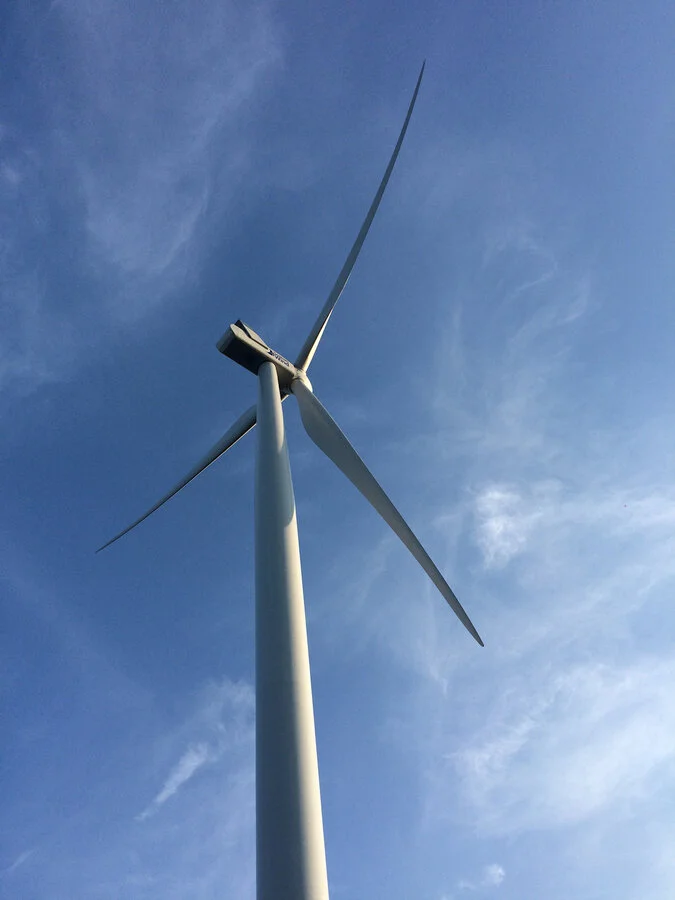 Close-up of a large wind turbine against a blue sky with wispy clouds.
