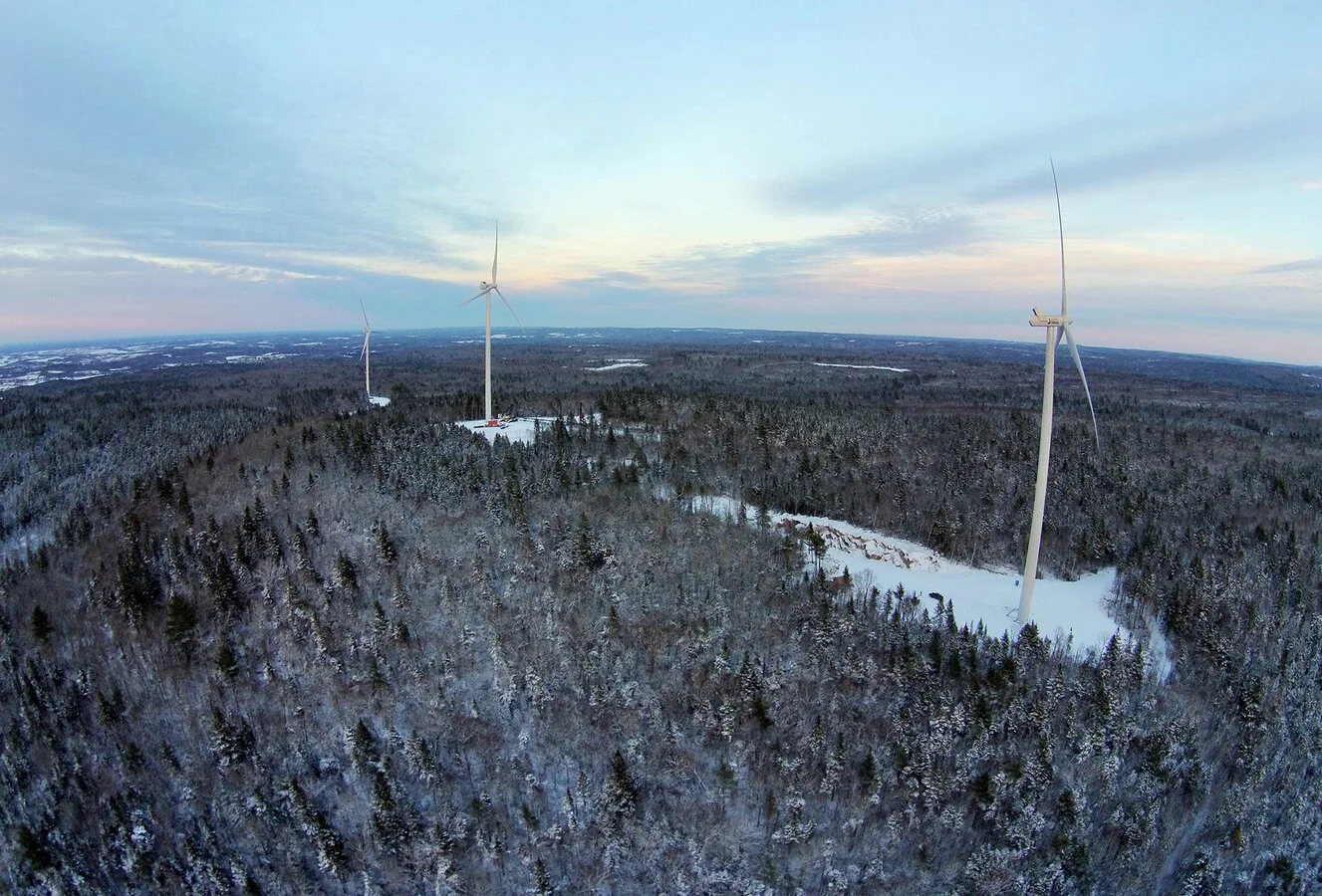 Aerial view of a snowy forest landscape with three wind turbines during the daytime.