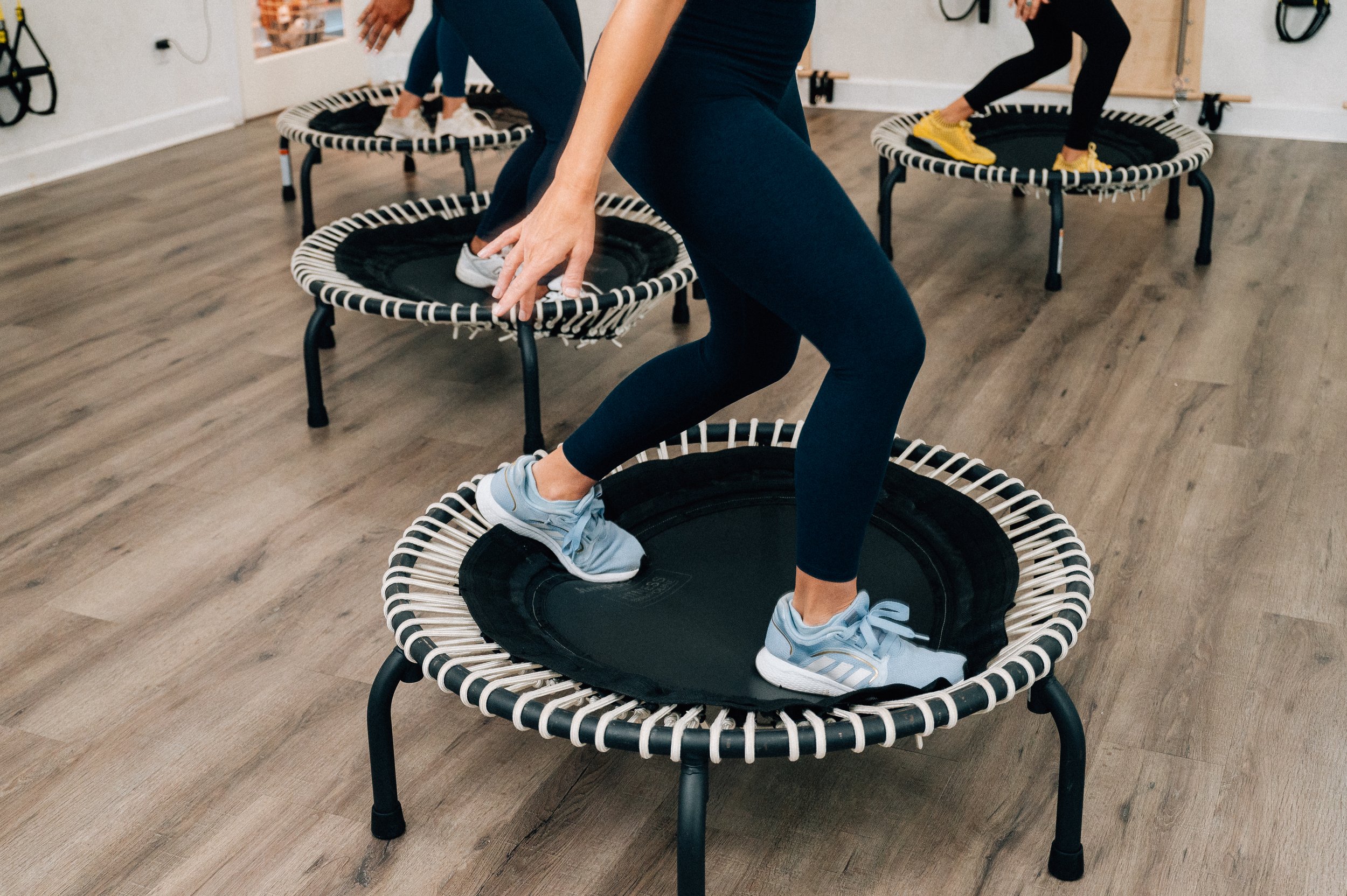 People exercising on small trampolines/rebounders indoors, wearing athletic clothing.
