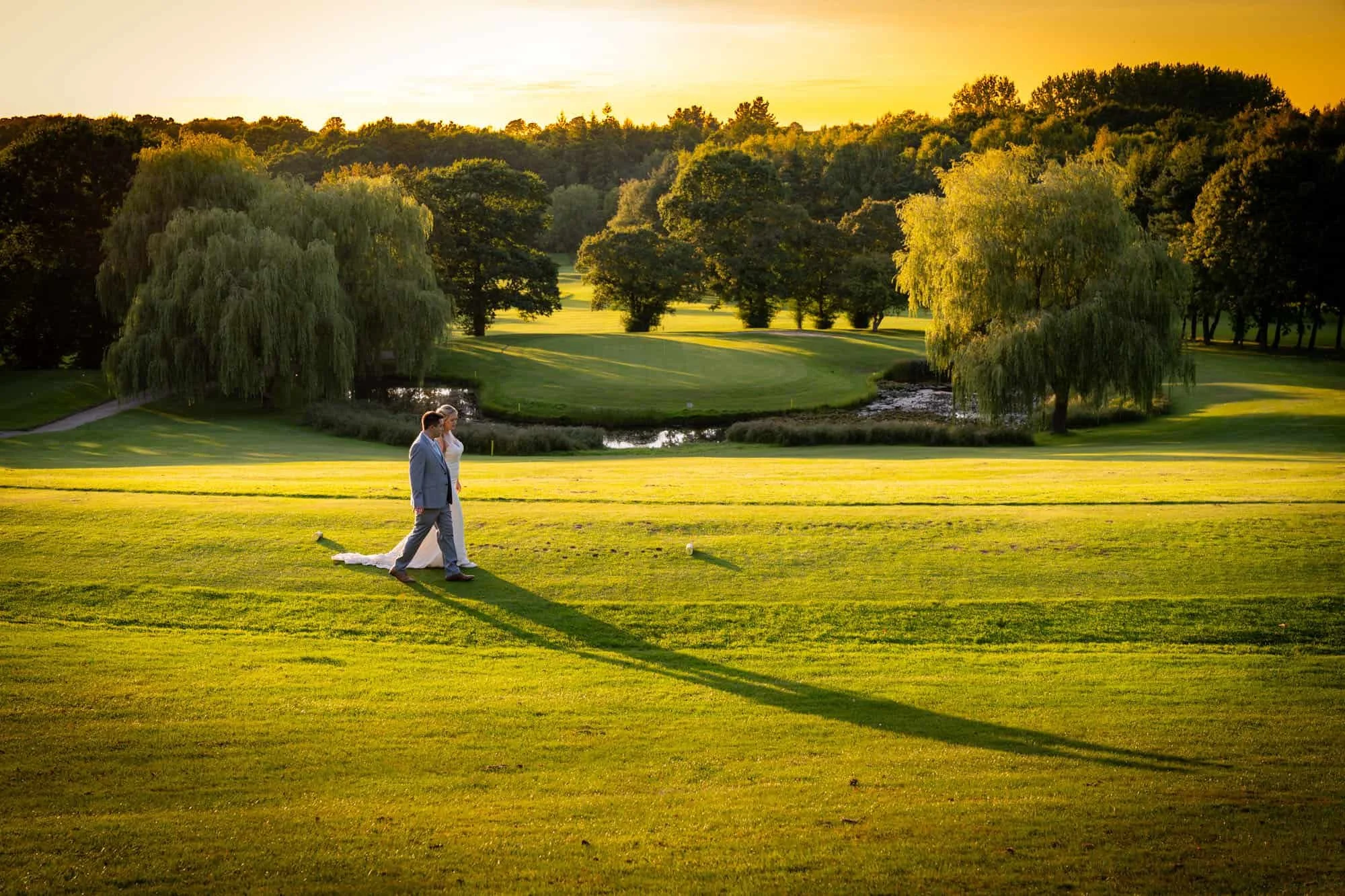 A bride and groom walking on a golf course during sunset.