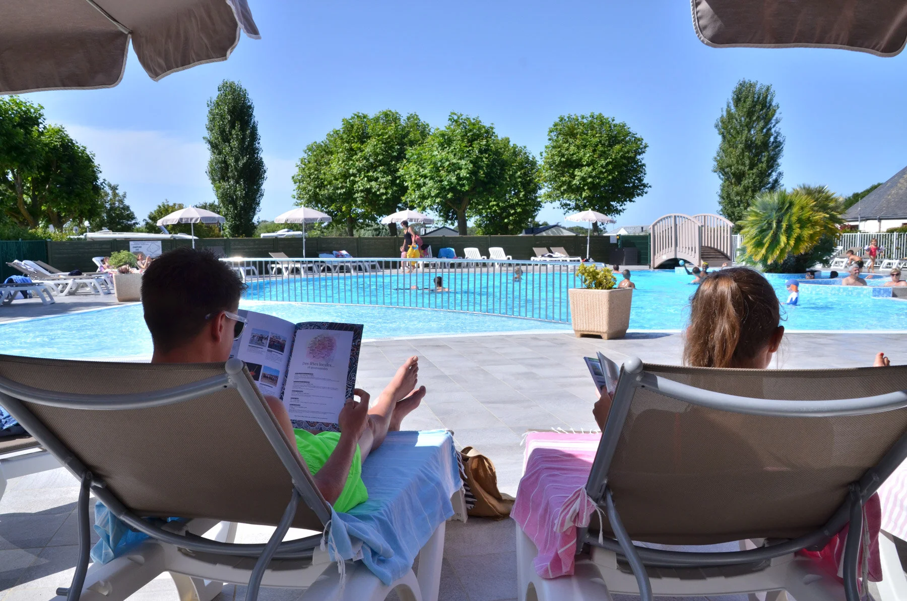Paar auf Sonnenliegen mit Blick auf den beheizten Pool des Camping Les Druides