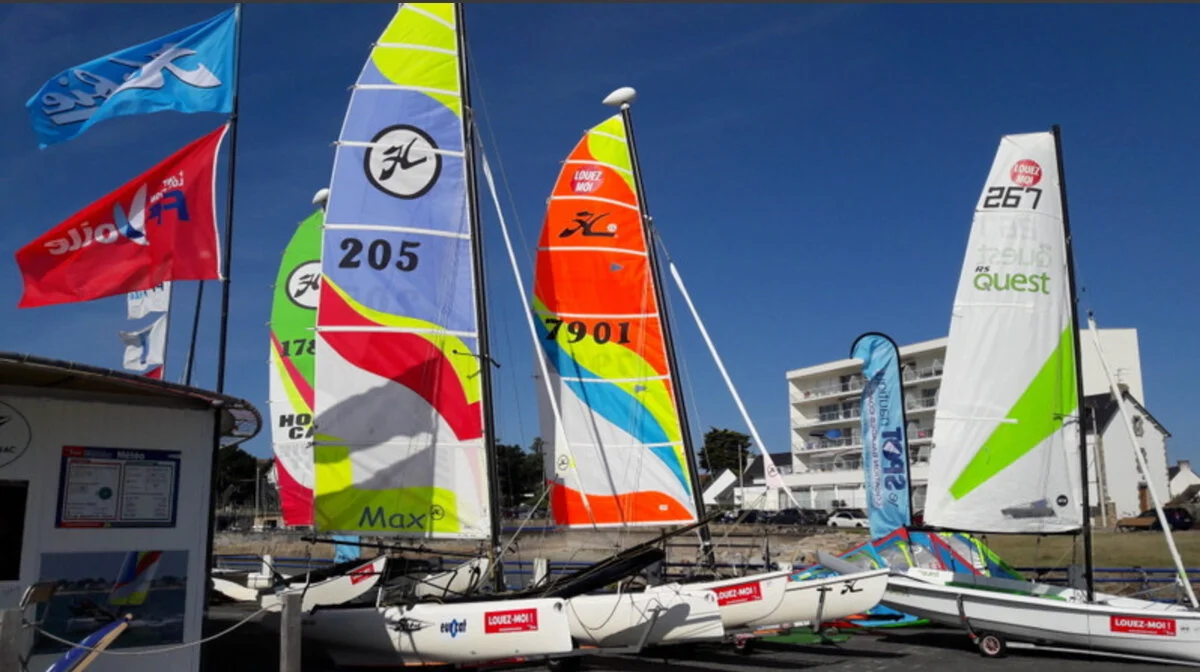 Catamarans with multicoloured sails lined up on the beach at Yacht Club Carnac in Port-en-Dro