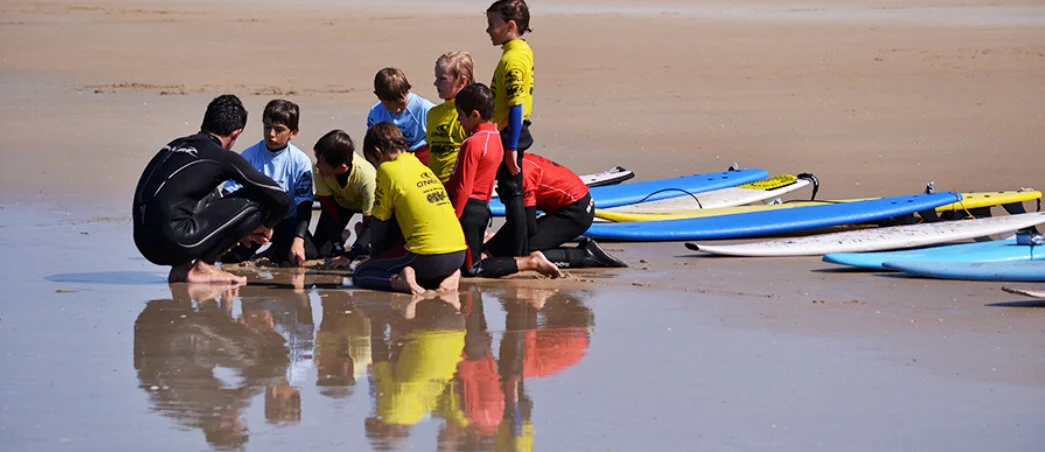 An instructor explaining the basics of surfing to a group of children on the wet sand, Plouharnel