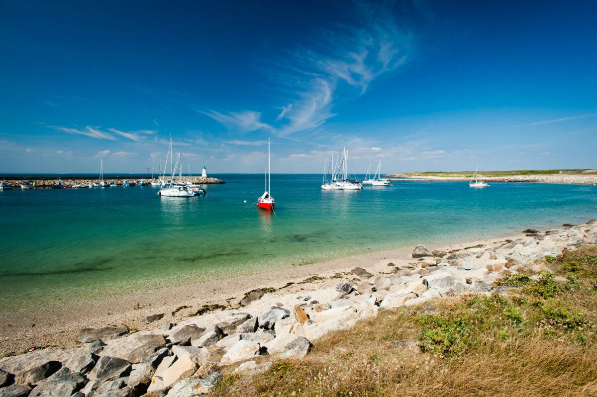 A cove with white sand, rocks and sailing boats at anchor on the island of Houat, Morbihan