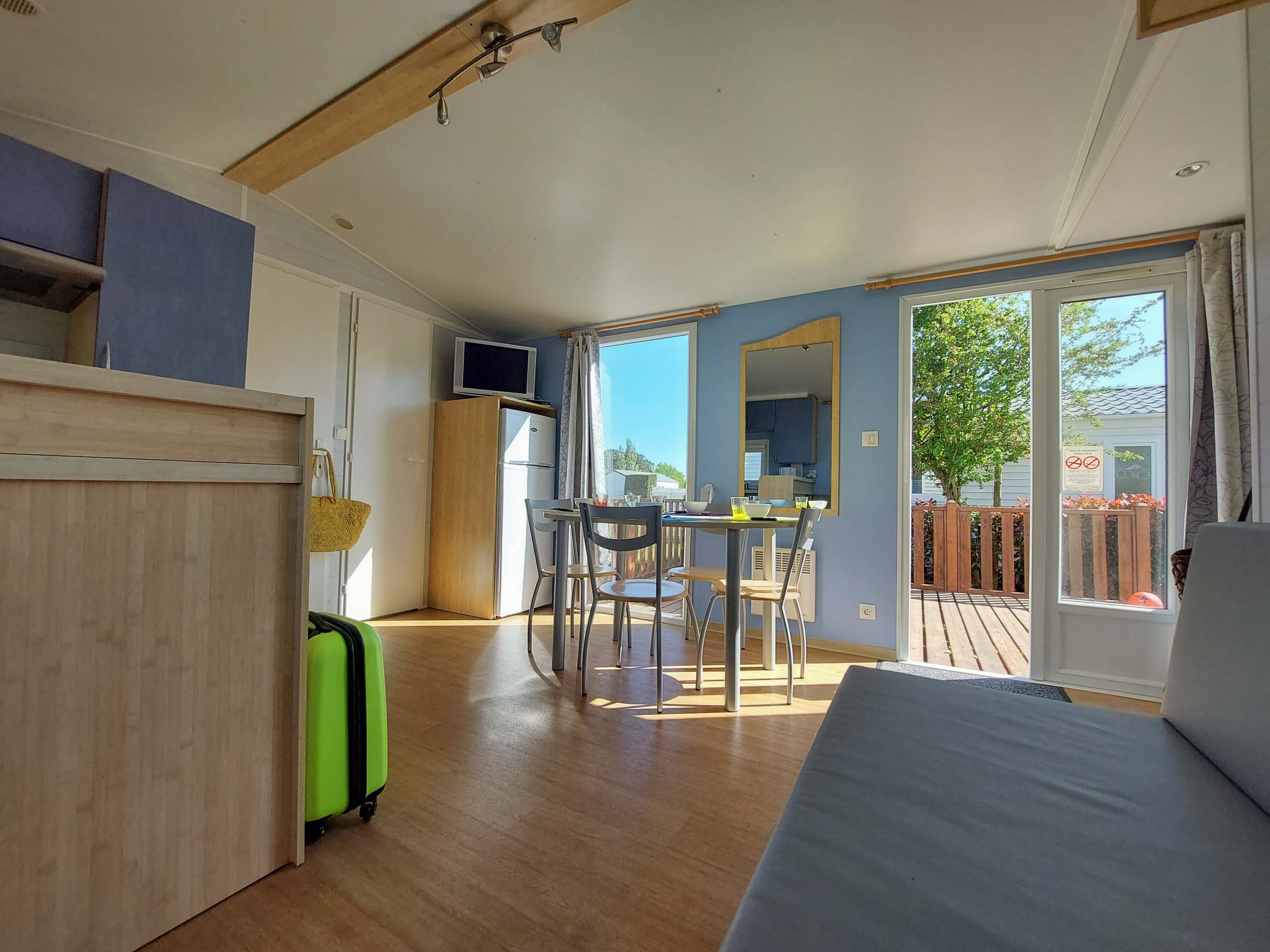Wohnbereich des Mobilheims Florès mit Esstisch und geöffneter Terrassentür zur Holzterrasse