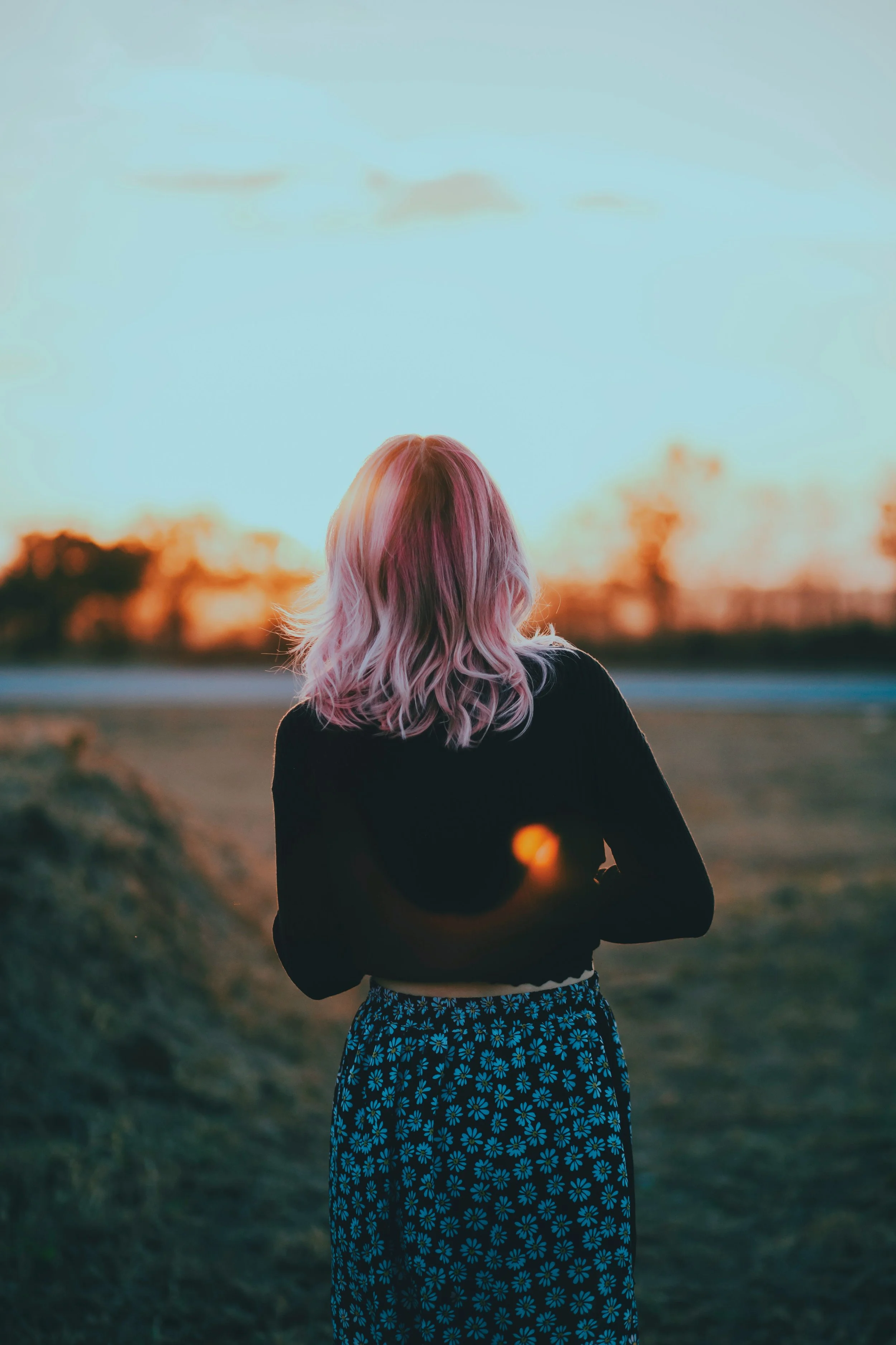 Young woman with pink hair in a field looking out into the distance
