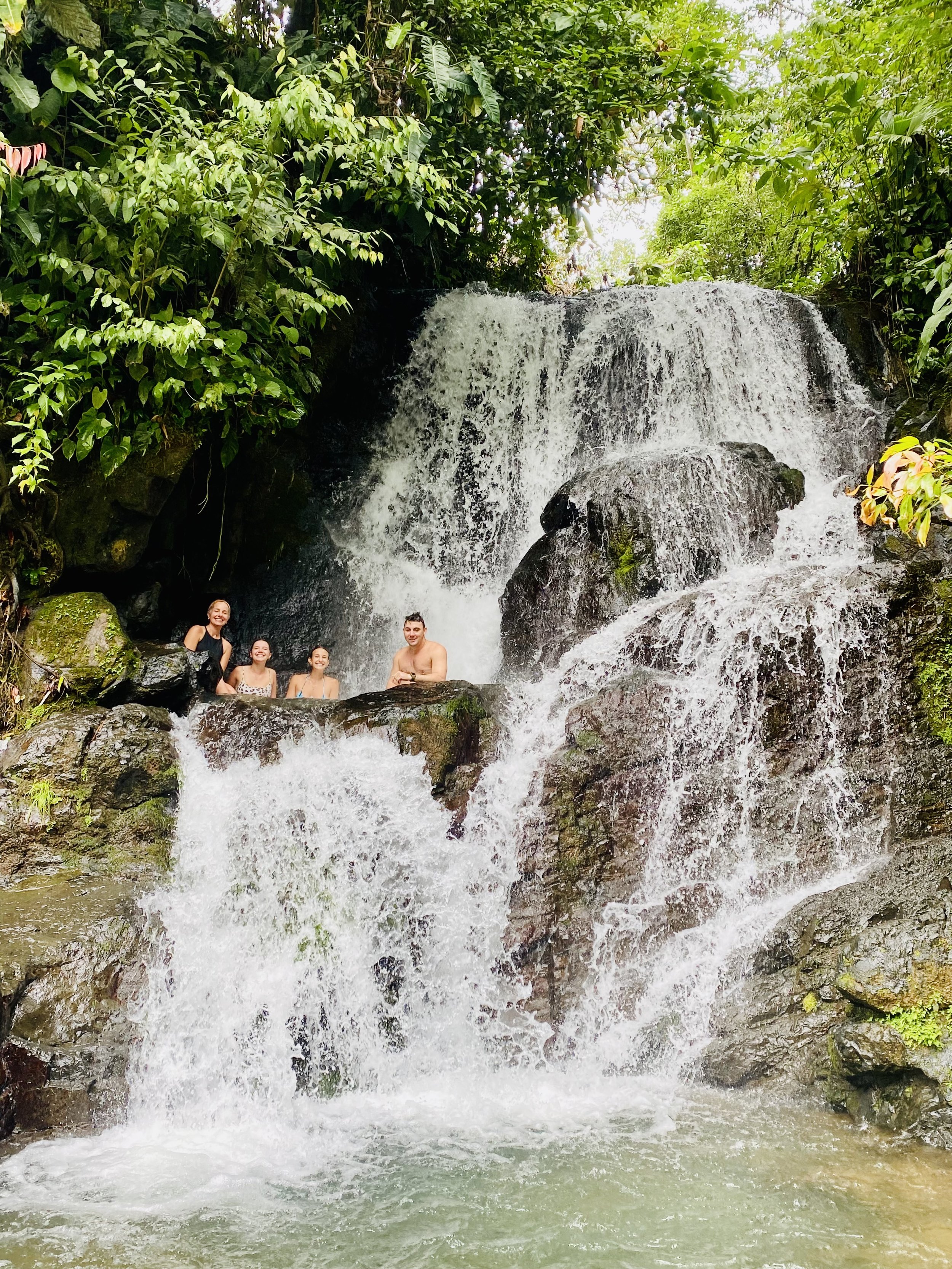 Guests swimming and relaxing beneath a natural rainforest waterfall at Chorro Ecolodge near Manuel Antonio, Costa Rica.
