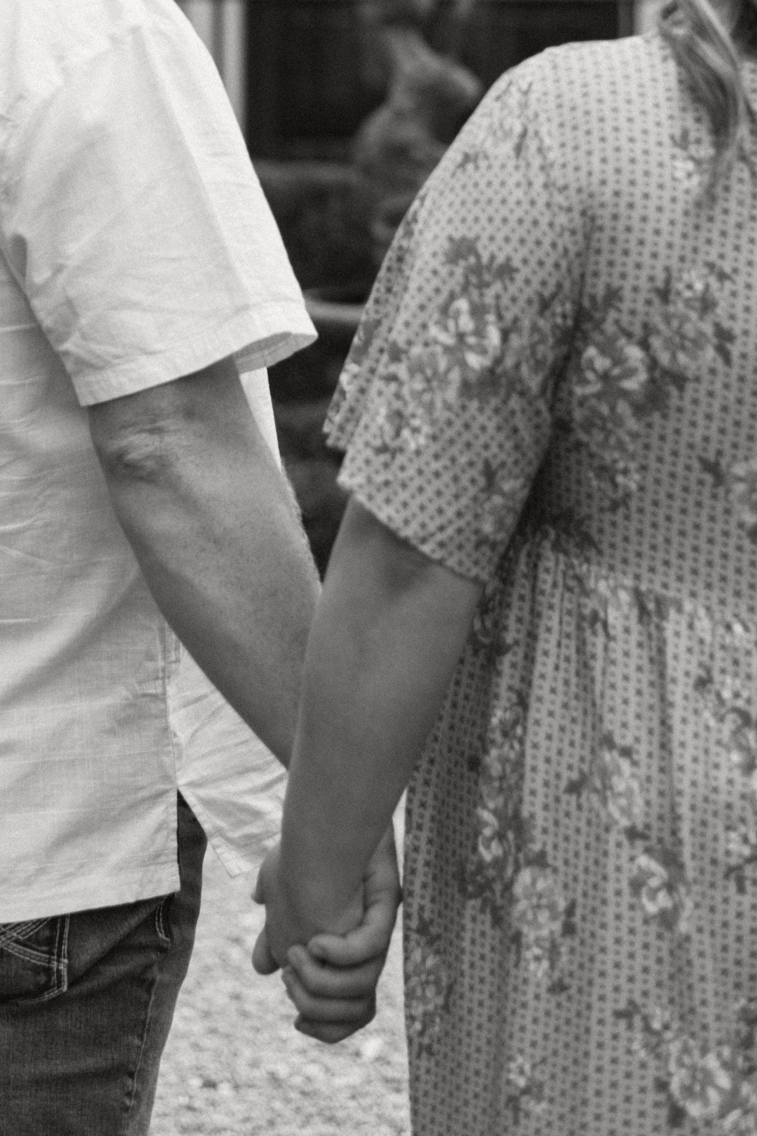 a black and white image of a couple holding hands outside, cropped closely so you can't see their faces