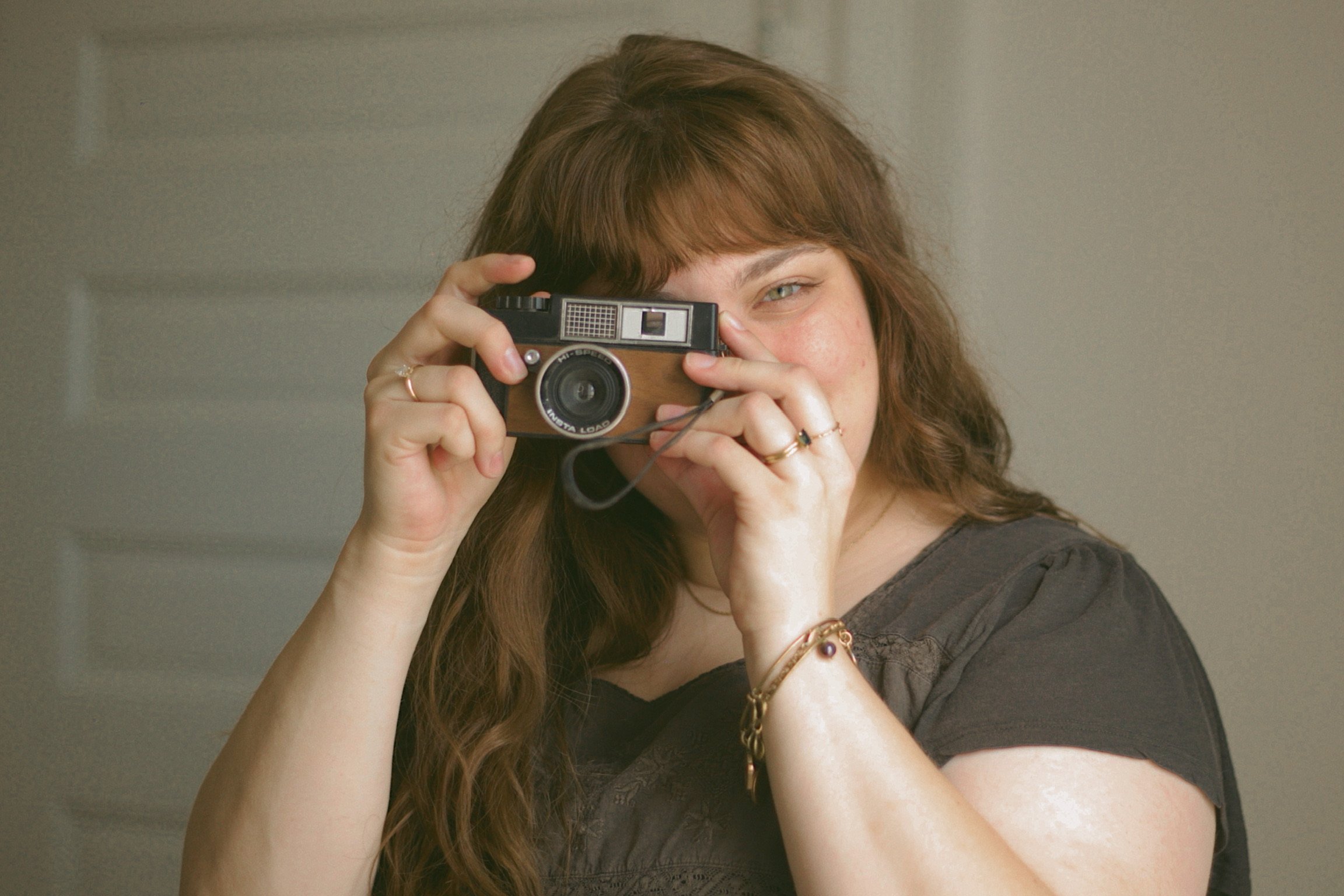 an indiana wedding and boudoir photographer holds up a vintage 35 mm camera, pointing it towards the lens. Her exposed eye looks directly into the lens, ready to take your picture