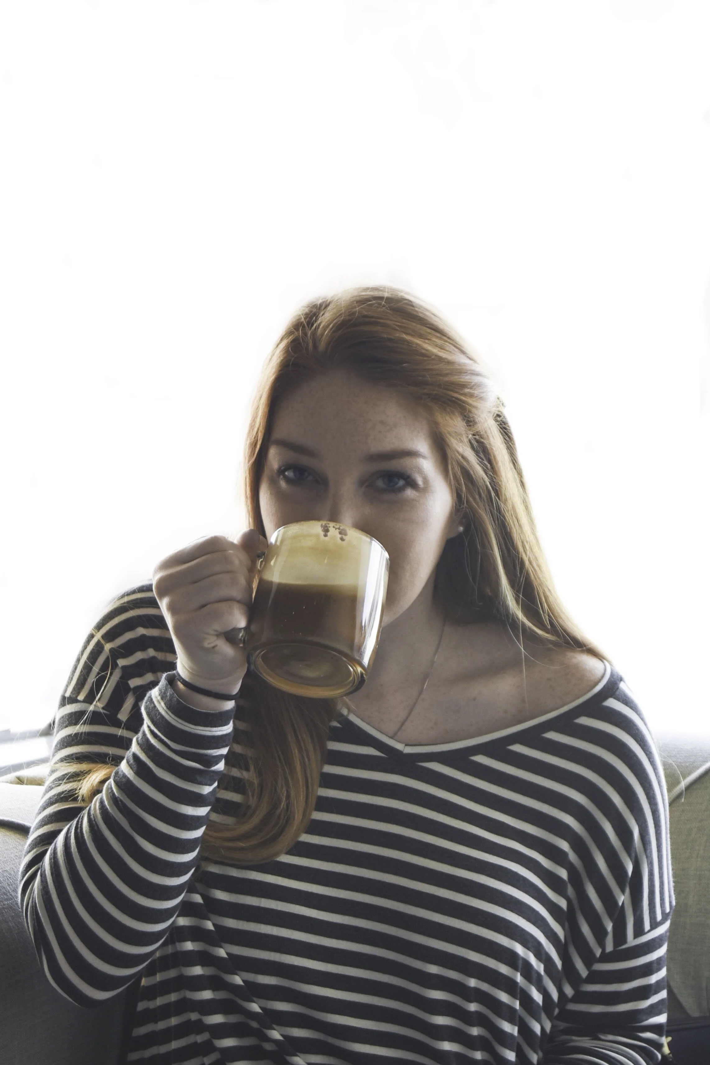Red headed woman in a striped shirt sipping a latte out of a glass mug