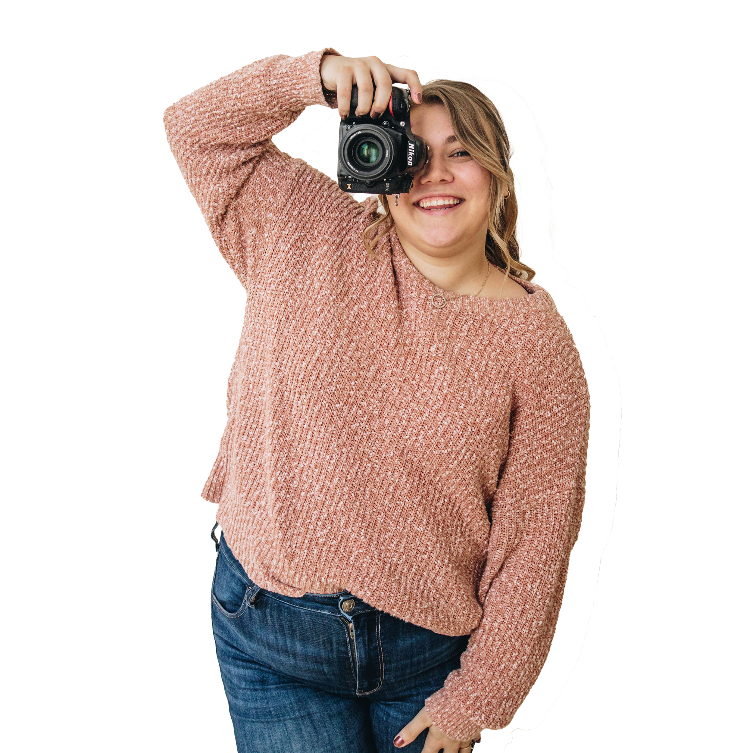 smiling blonde woman in jeans and a sweater holding a Nikon D750 in front of one eye as if taking your photo