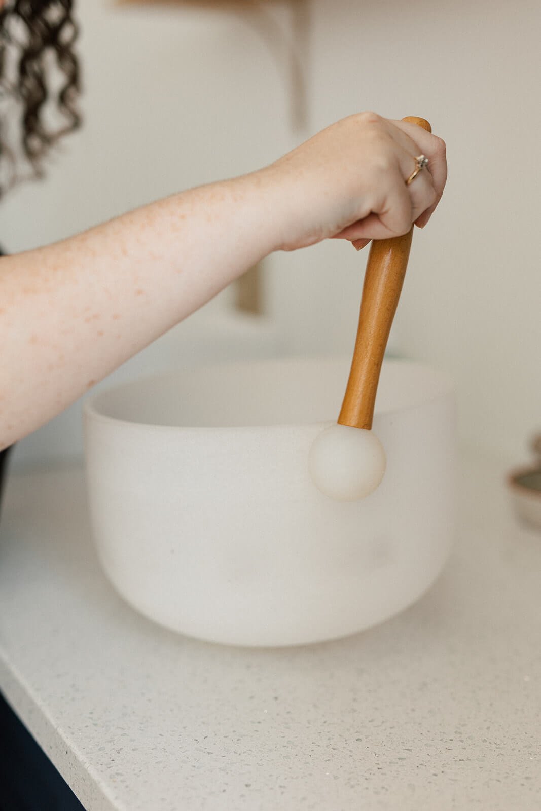 A person using a wooden mallet to play a frosted crystal singing bowl on a countertop.