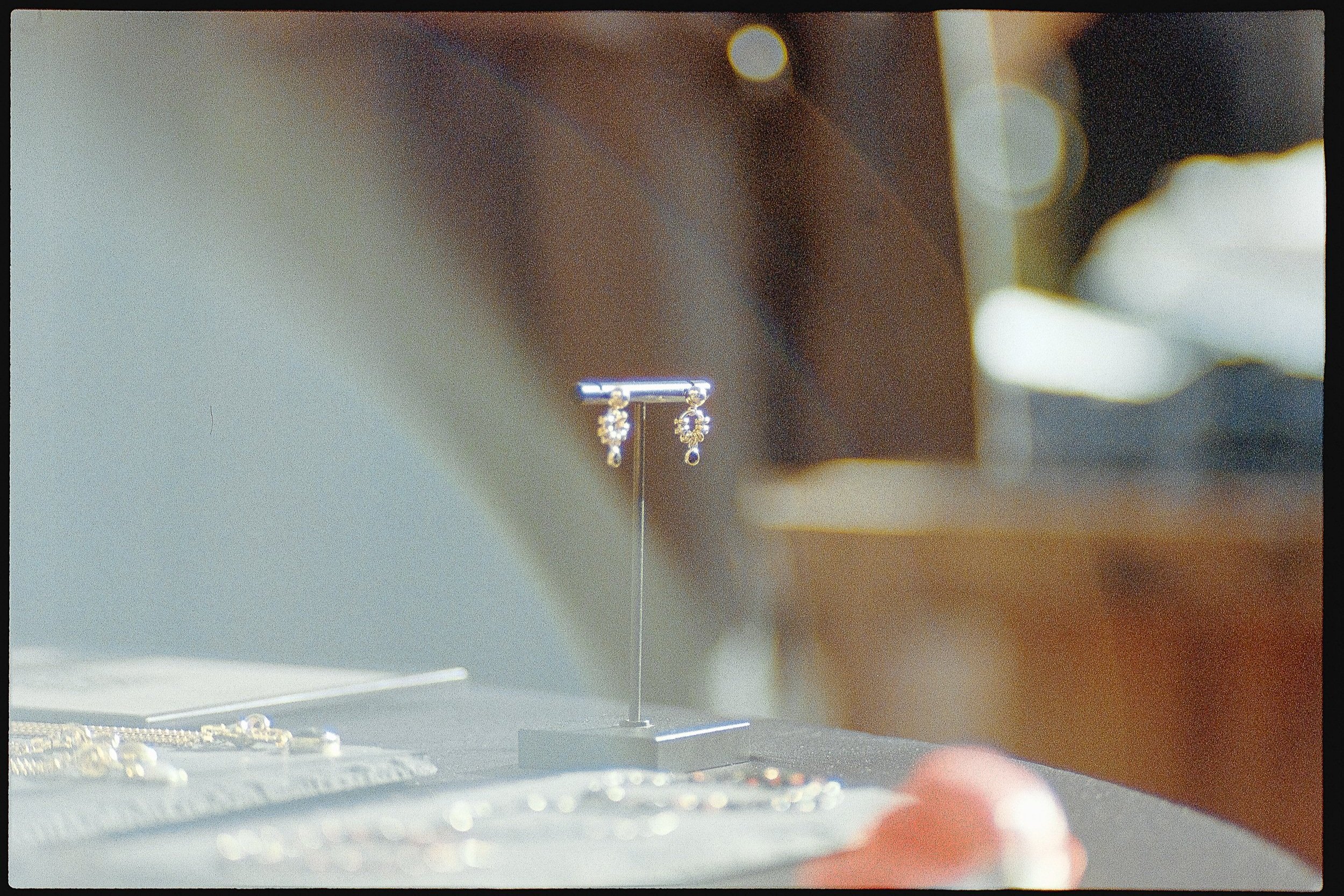 A pair of elegant earrings displayed on a stand at a jewelry store, with various jewelry pieces visible on a table in the background.
