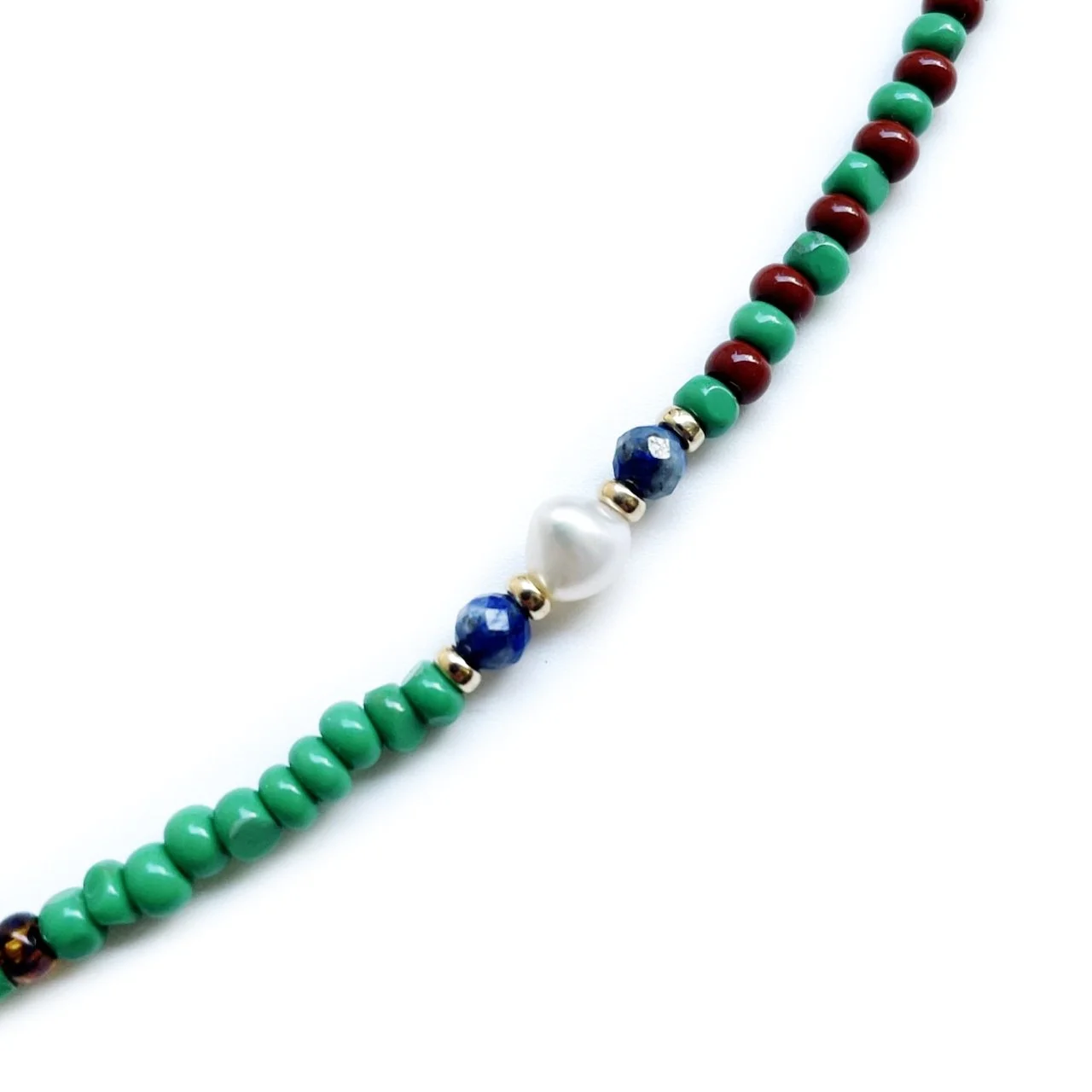 Close-up of a beaded necklace with green, red, blue, white, and gold beads arranged in a pattern on a white background.