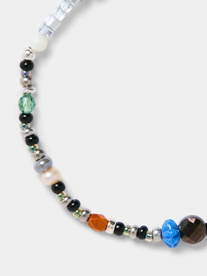 Close-up of a colorful beaded necklace with various sizes and shapes of beads, including black, white, silver, green, orange, blue, and brown beads, on a white background.