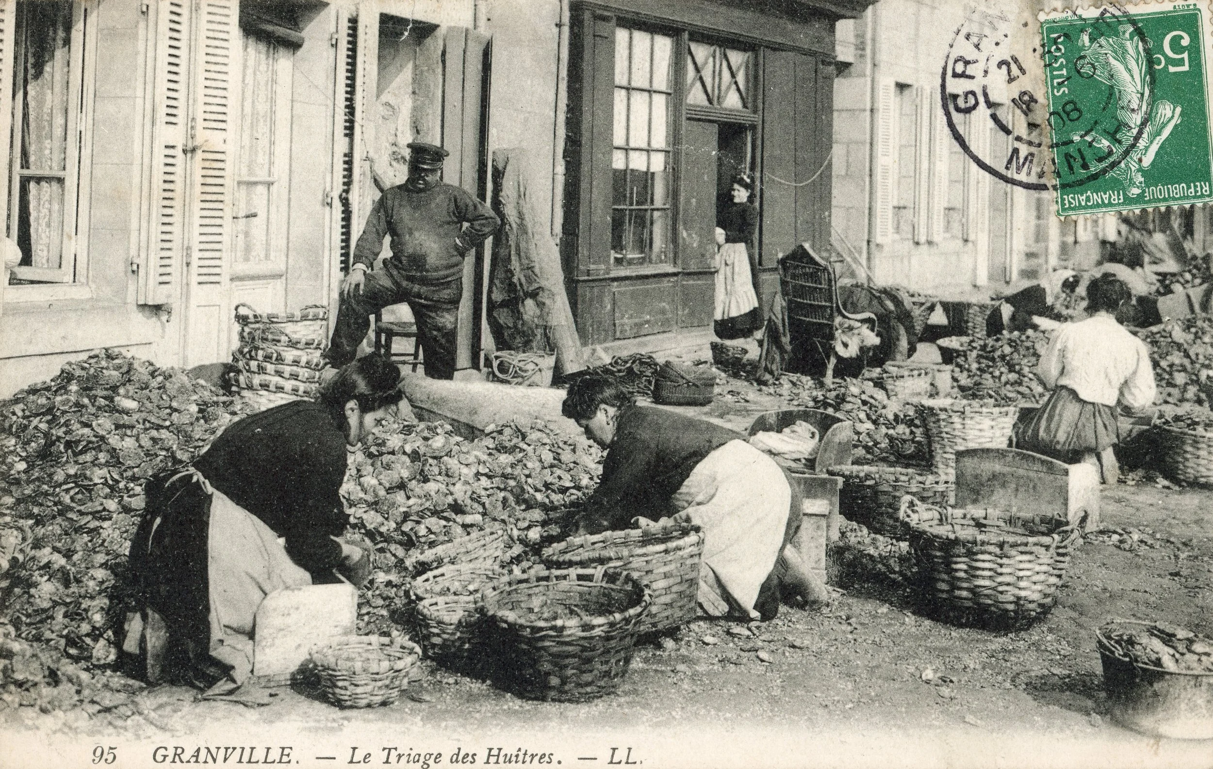 Femmes en train de trier des huîtres dans une rue de Granville, France, dans une scène historique en noir et blanc.
