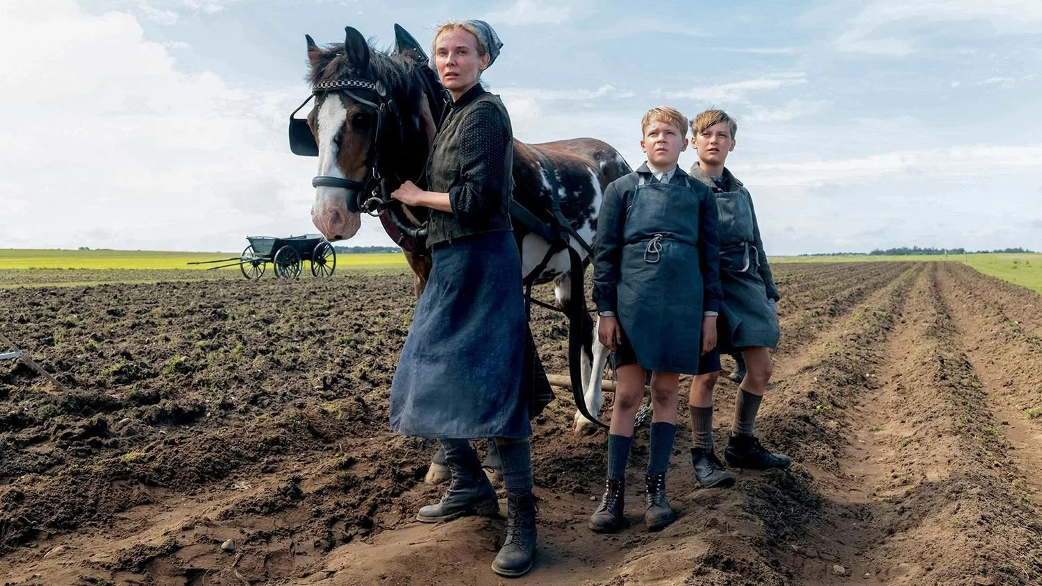 Eine Frau steht mit zwei Jungen und einem Pferd während der Arbeit auf einem Acker