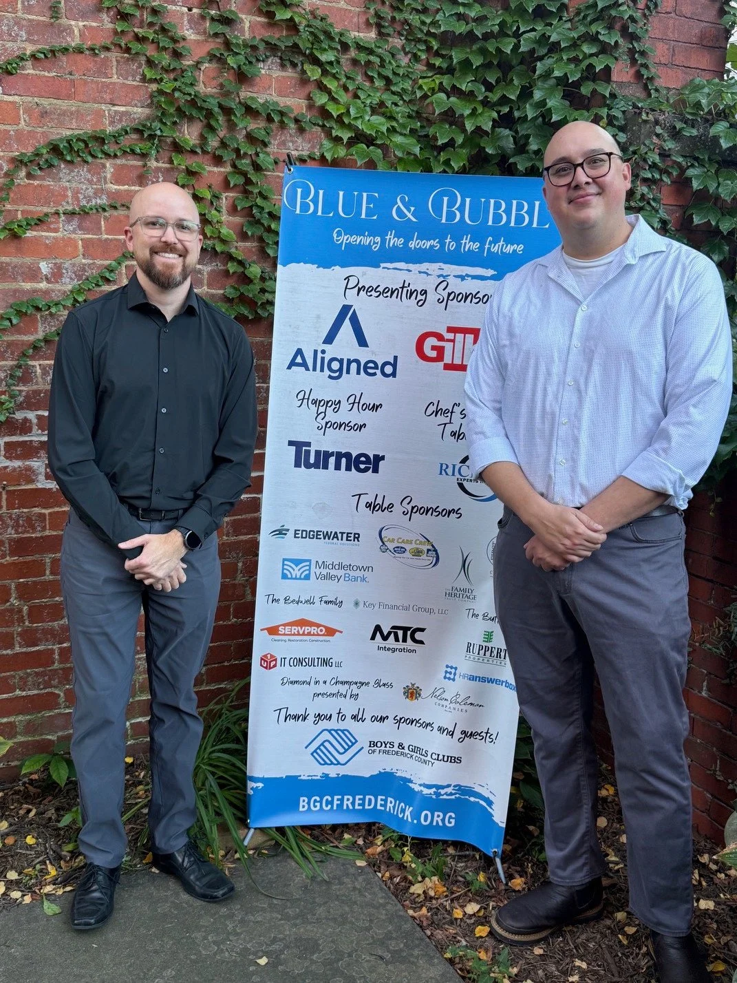 Two event attendees beside the Blue & Bubbly sponsor banner for Boys & Girls Clubs of Frederick County.