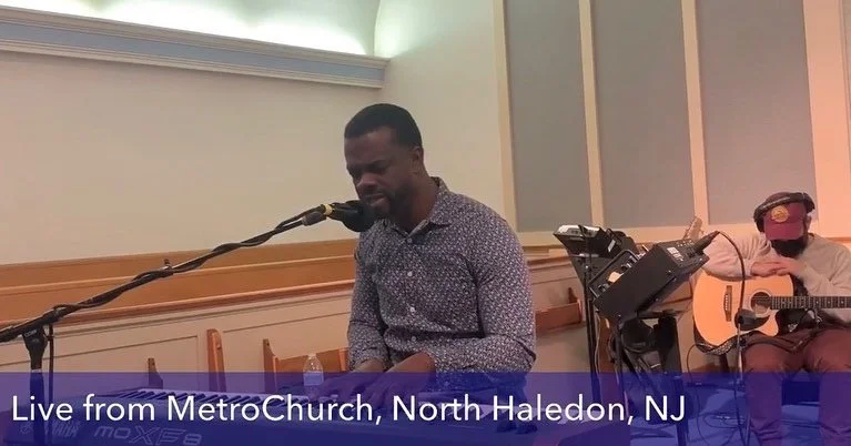 Musicians performing live at MetroChurch in North Haledon, New Jersey, with one person singing and playing piano, and another person playing guitar.