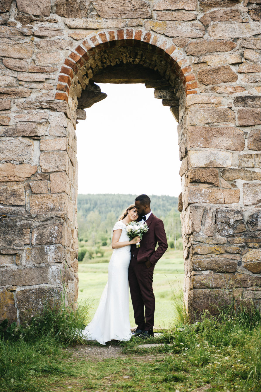 Brudepar står tett sammen i steinbuen ved ruinene av Margaretakirken i Oslo, et romantisk bryllupsportrett i historiske omgivelser.