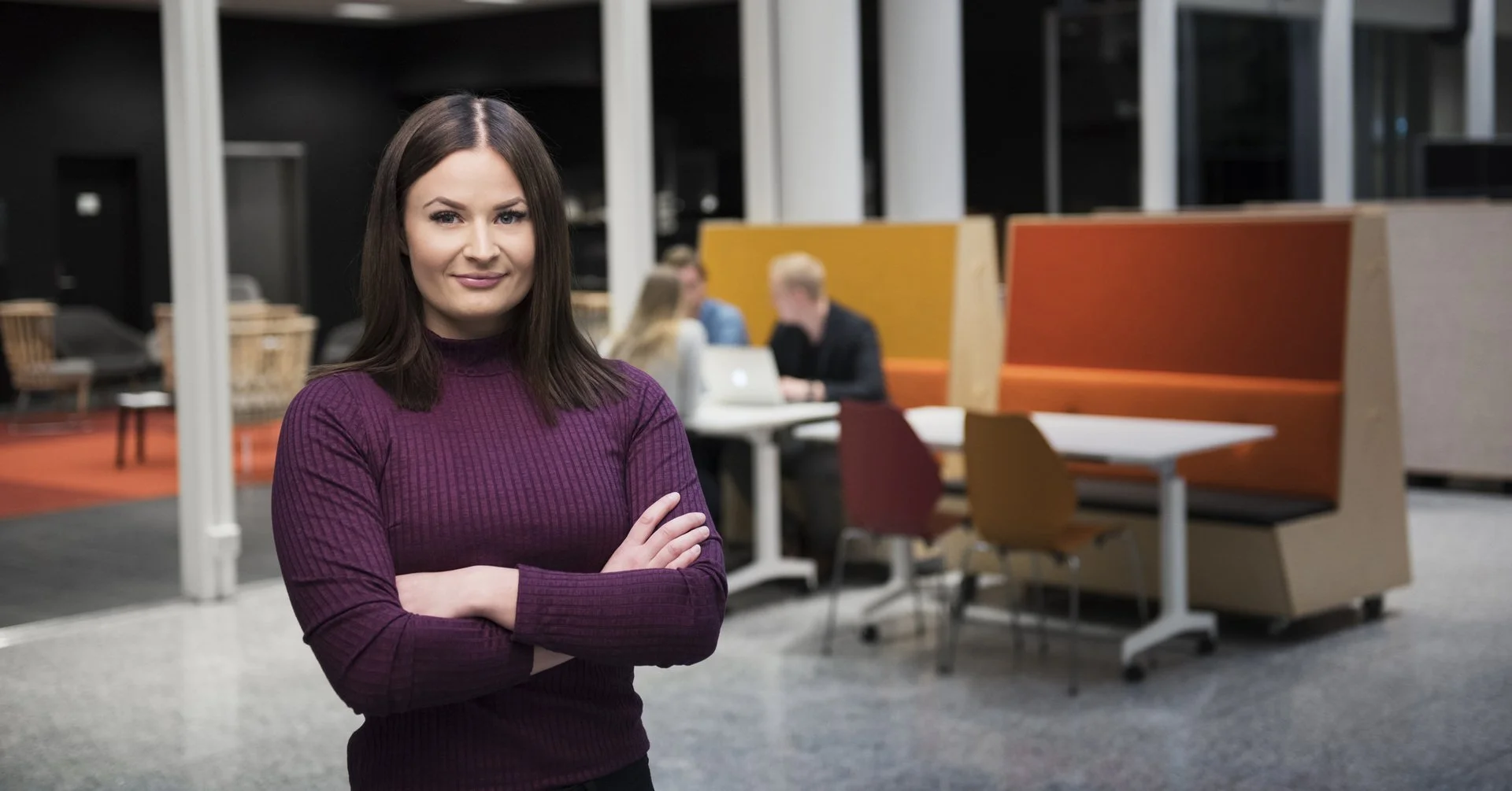 Miljøportrett av en kvinne med armene i kors i et moderne studiemiljø for Høyskolen Kristiania.