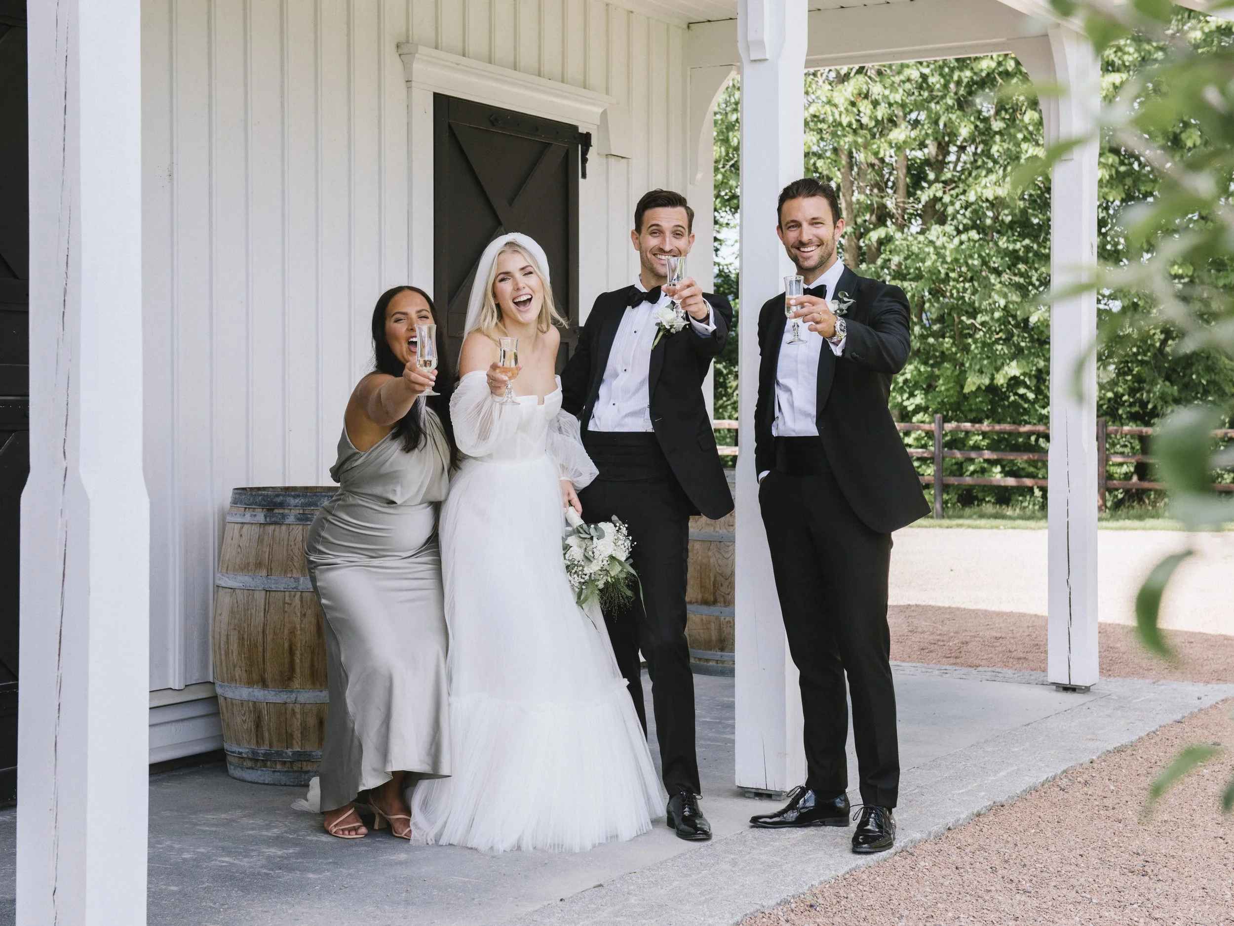 Brudepar og venner skåler og feirer sammen på gårdstunet ved Svensefjøset i Lier, et livlig og ekte øyeblikk fra bryllupsdagen.