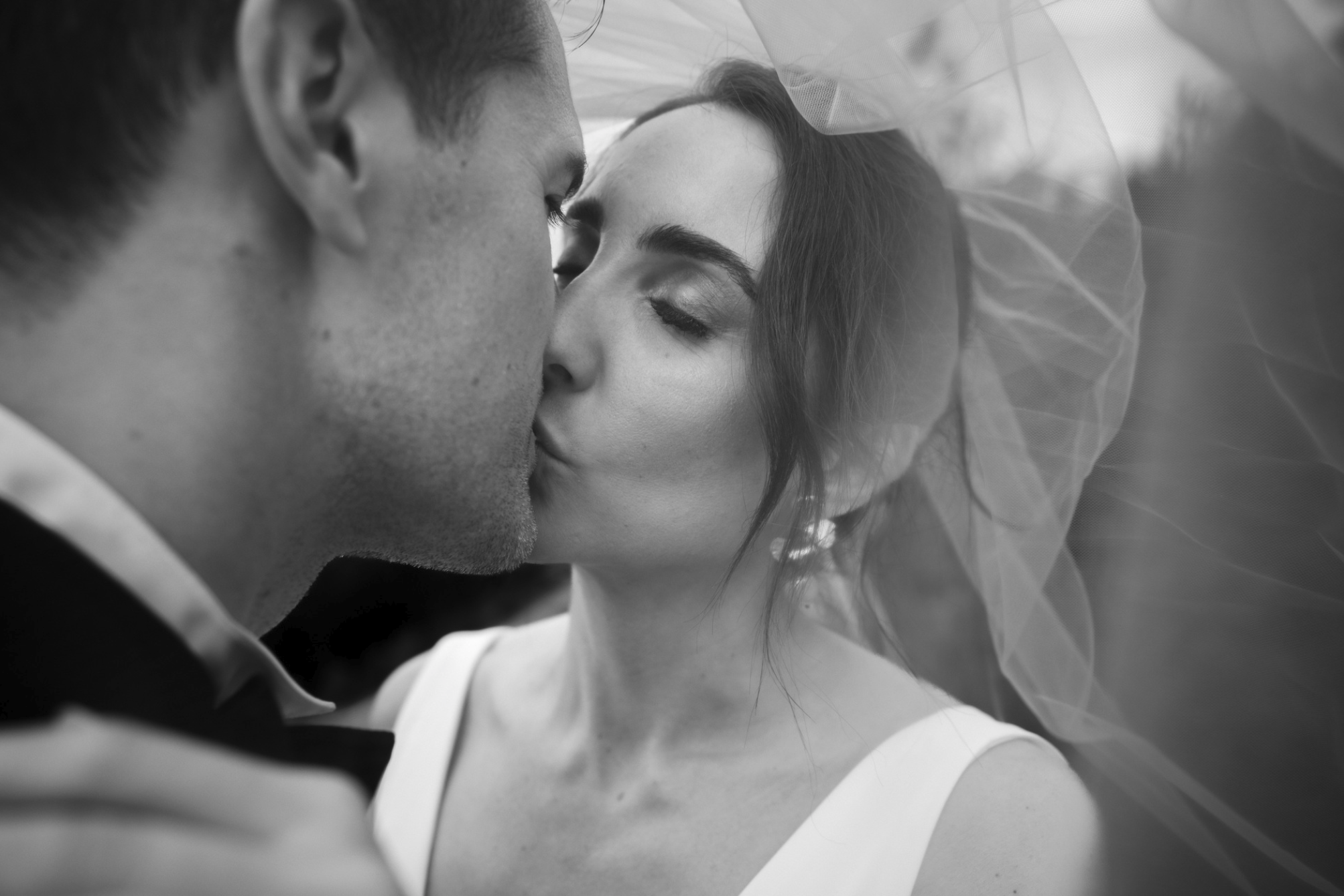 Nært og romantisk øyeblikk av brudepar som kysser under sløret, et kunstnerisk bryllupsportrett med mykt lys på Lysebu i Oslo.