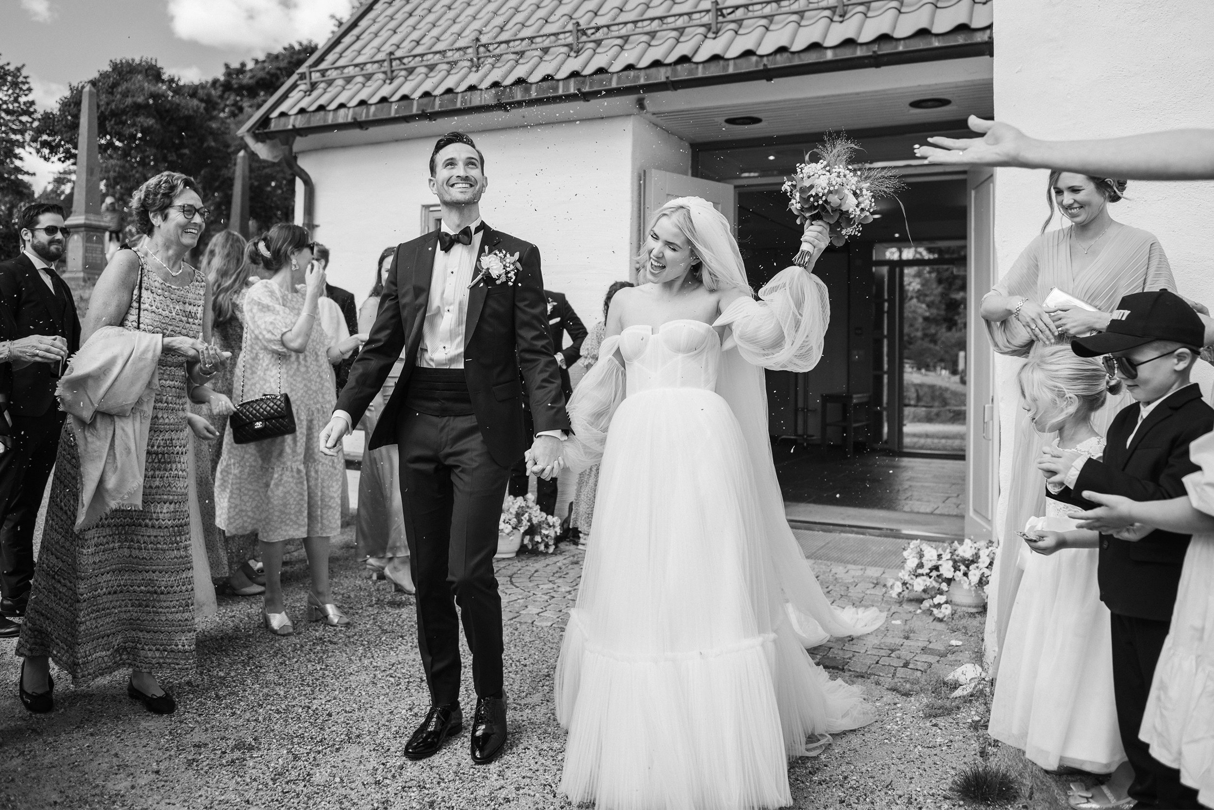 Brudepar går ut av kirken mens gjestene feirer rundt dem, et livlig og dokumentarisk øyeblikk fra bryllupet i Lier.