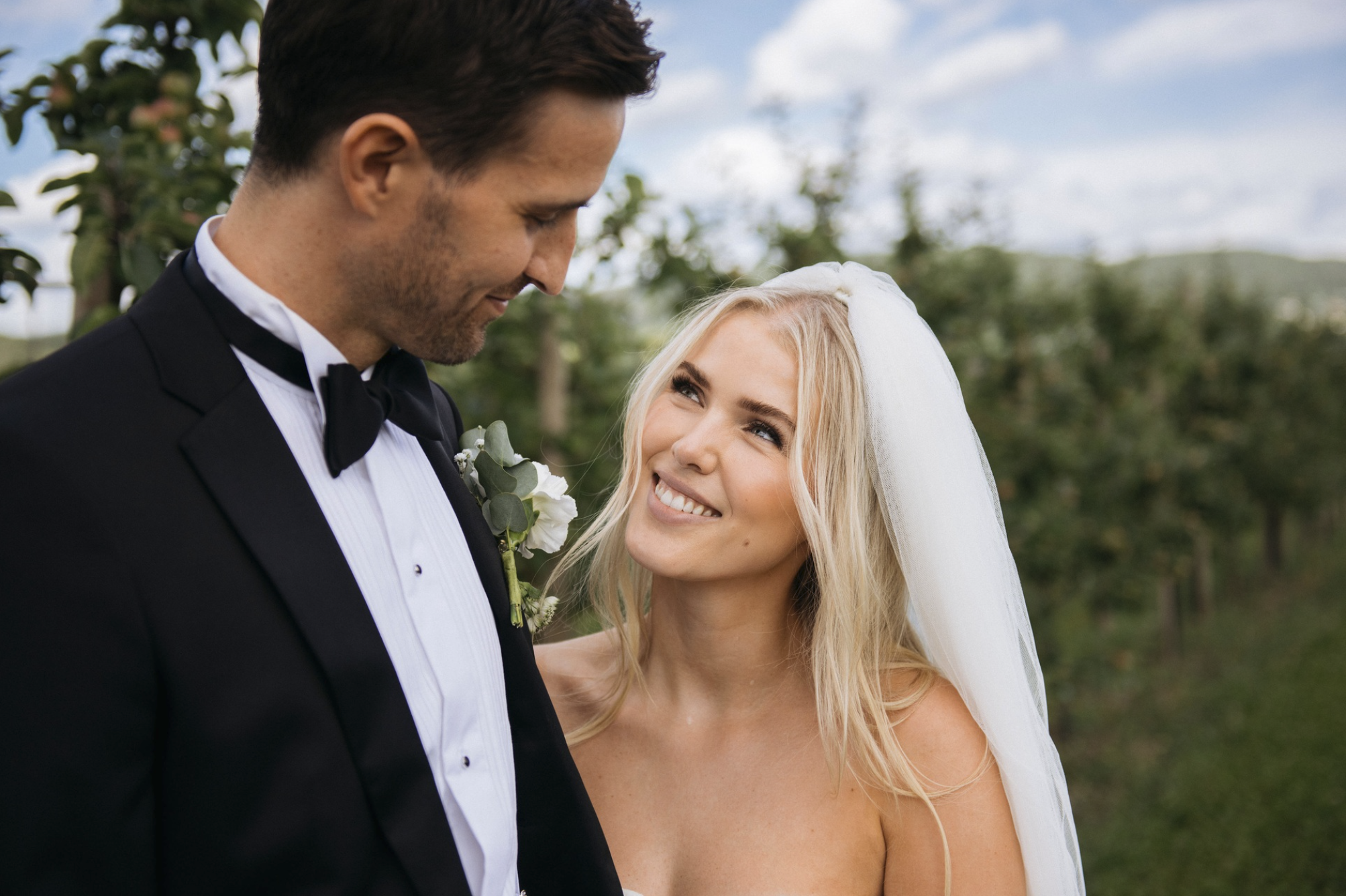 Brudepar i Lier står i frukthagen og ser kjærlig på hverandre, et lyst og naturlig bryllupsportrett i sommerlys.