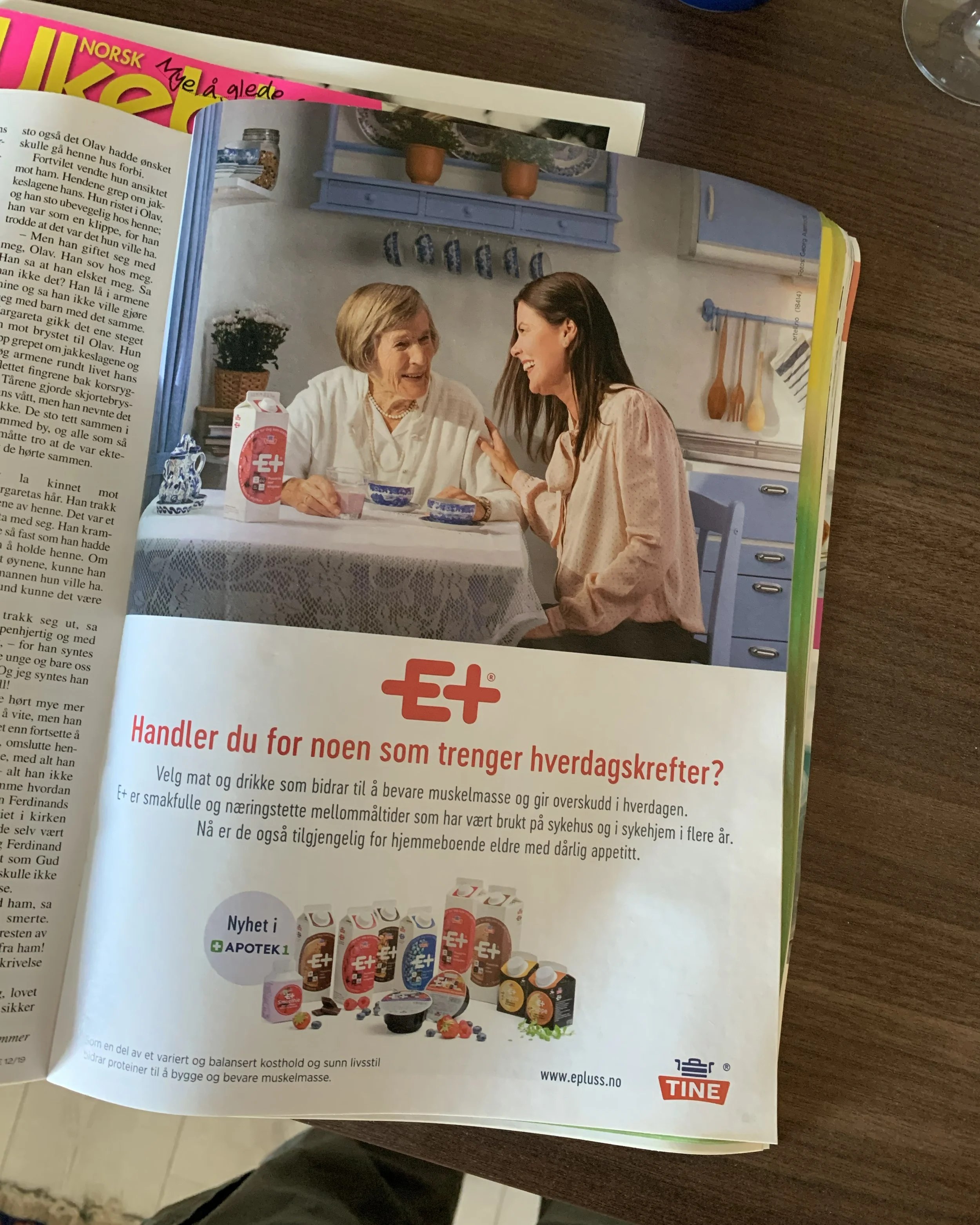 Kampanjebilde for TINE E+ med eldre kvinne og yngre kvinne ved kjøkkenbord, brukt i trykt annonse for mellommåltider.