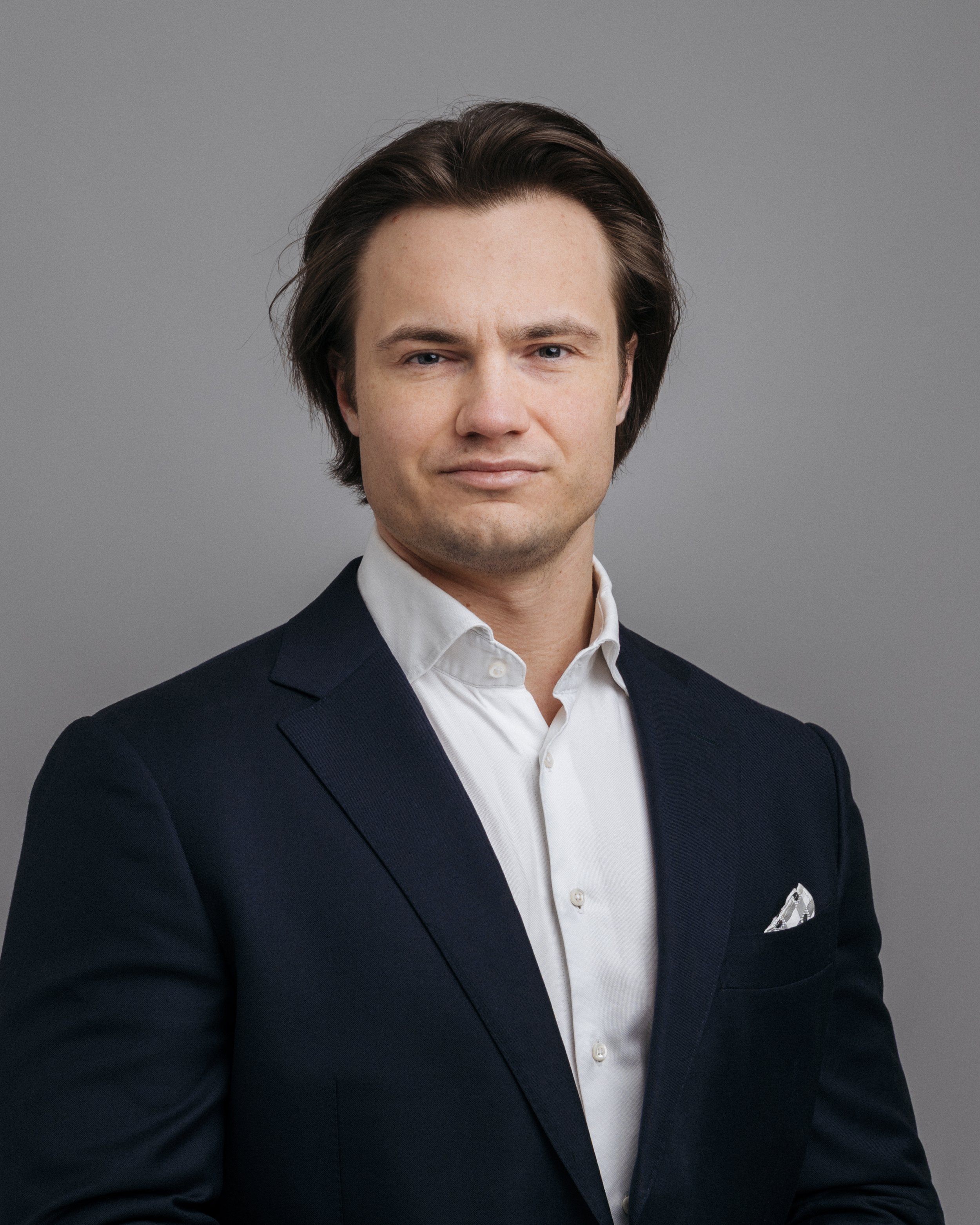 Portrett av en mann i dress mot en grå bakgrunn.