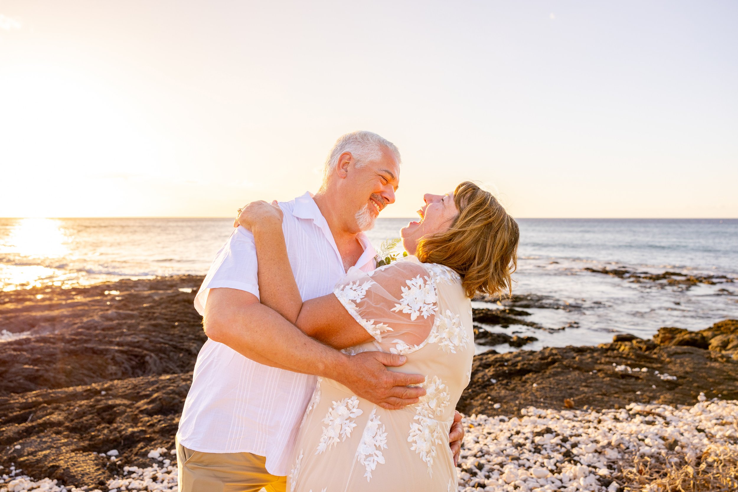 A happy older couple dancing and smiling on a rocky beach at sunset