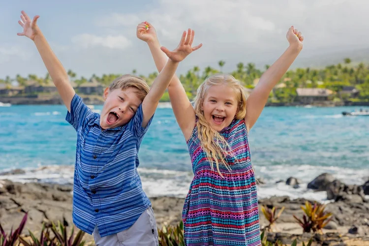 Two young kids sitting on beach with tidepools behind them