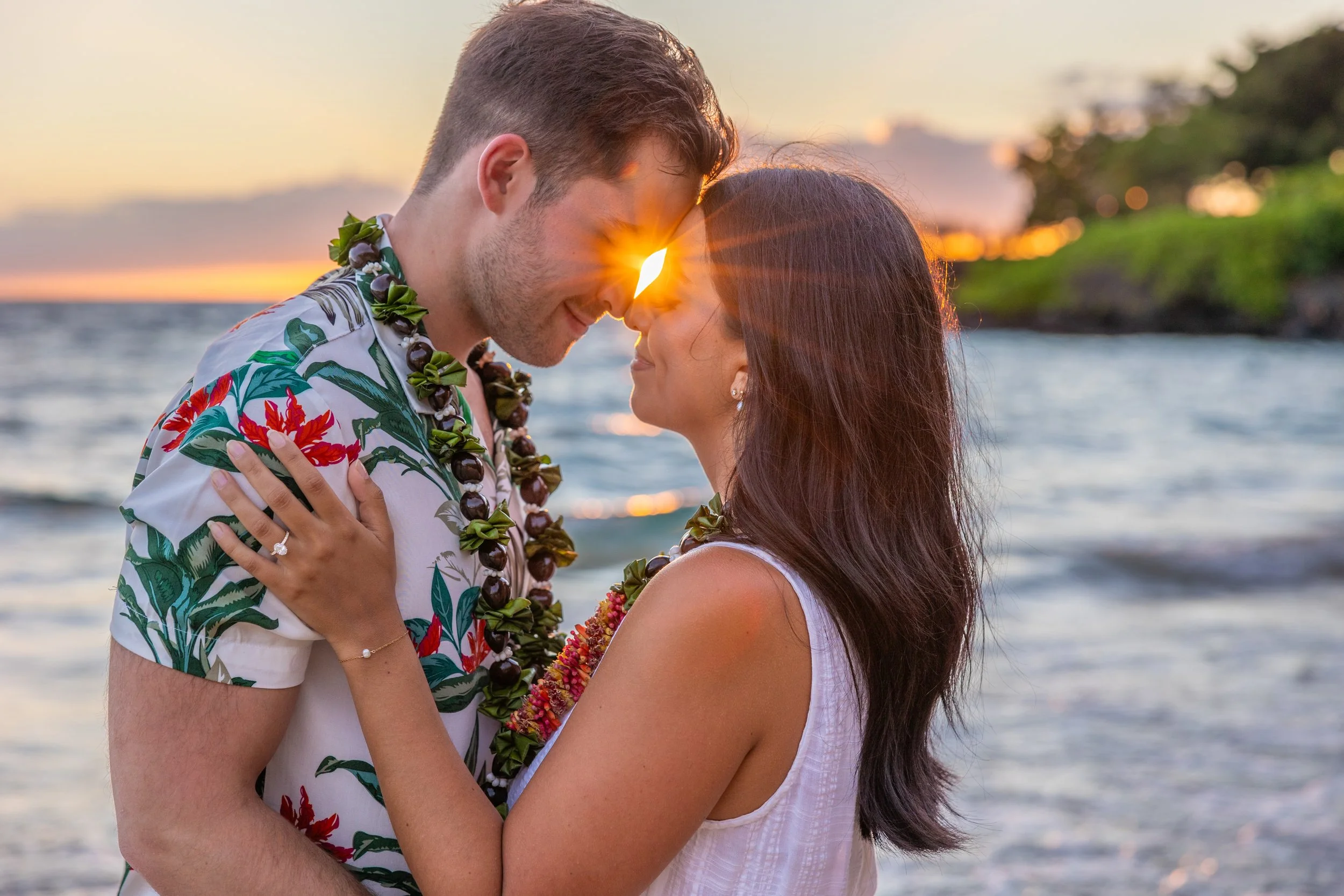 A couple embracing on the beach at sunset, with their foreheads touching and the sun shining through their noses.