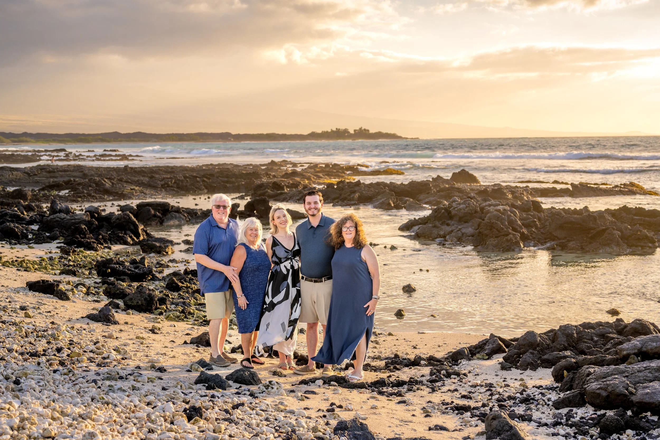 A group of five people standing on a rocky beach at sunset, smiling for the camera.