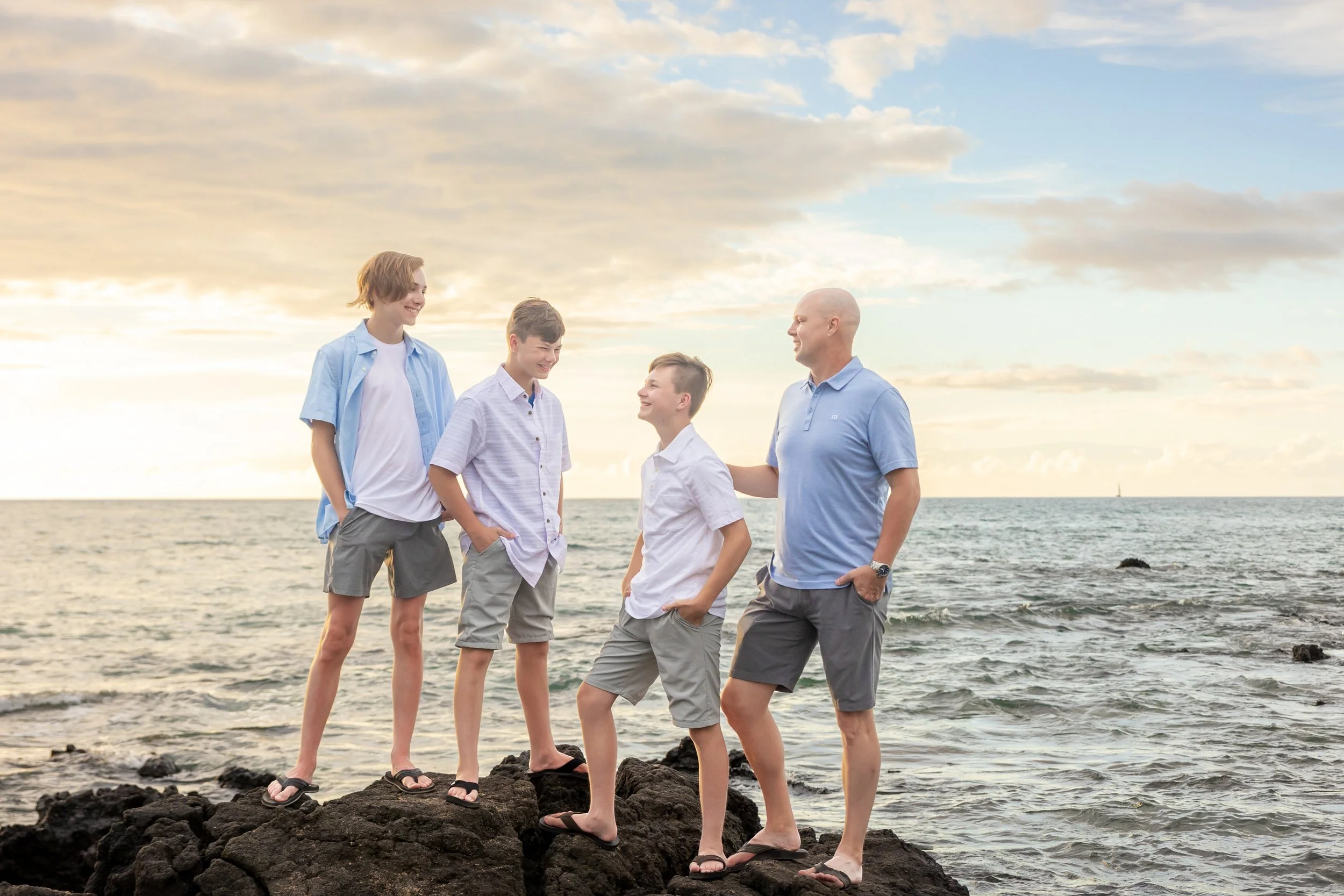 A family of five standing on rocks by the ocean during sunset, smiling and talking.