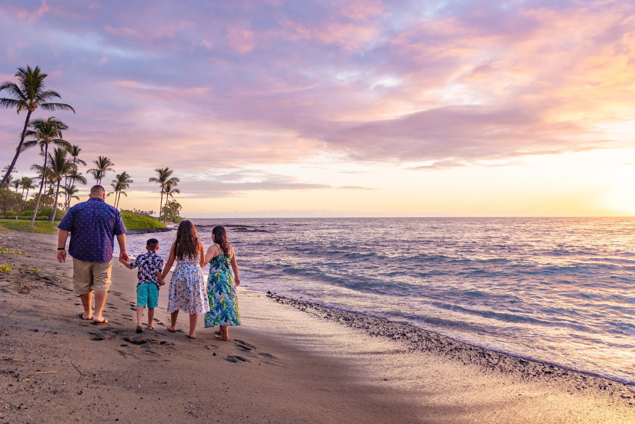 Family of five walking along the beach at sunset, with palm trees and ocean waves in the background.