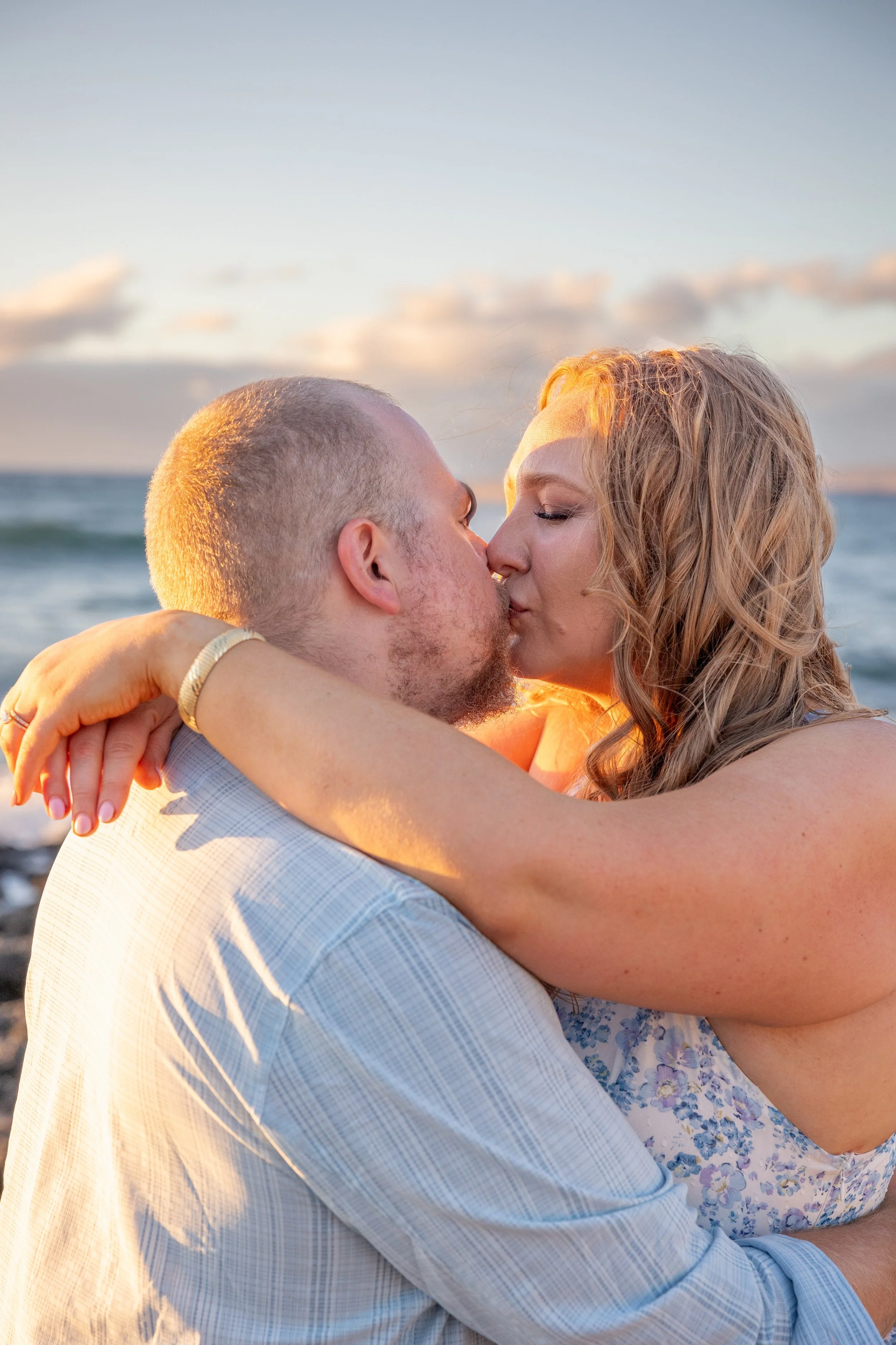 A man and woman kissing on the beach at sunset, with ocean waves in the background.