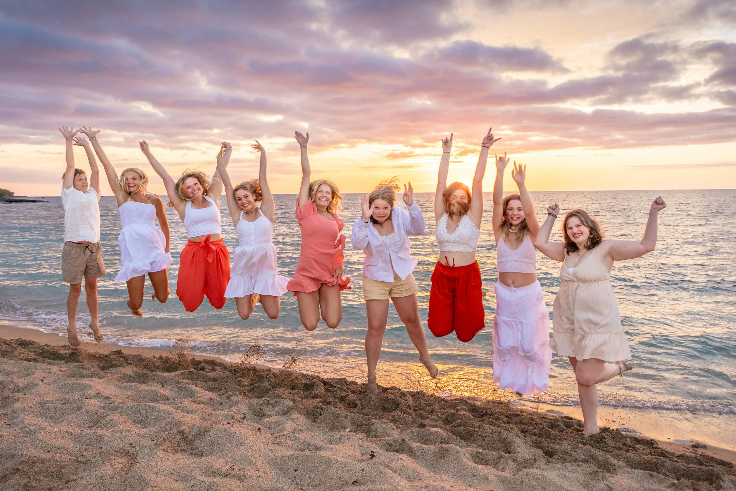 Ten women jumping on the beach during sunset, smiling and enjoying themselves.