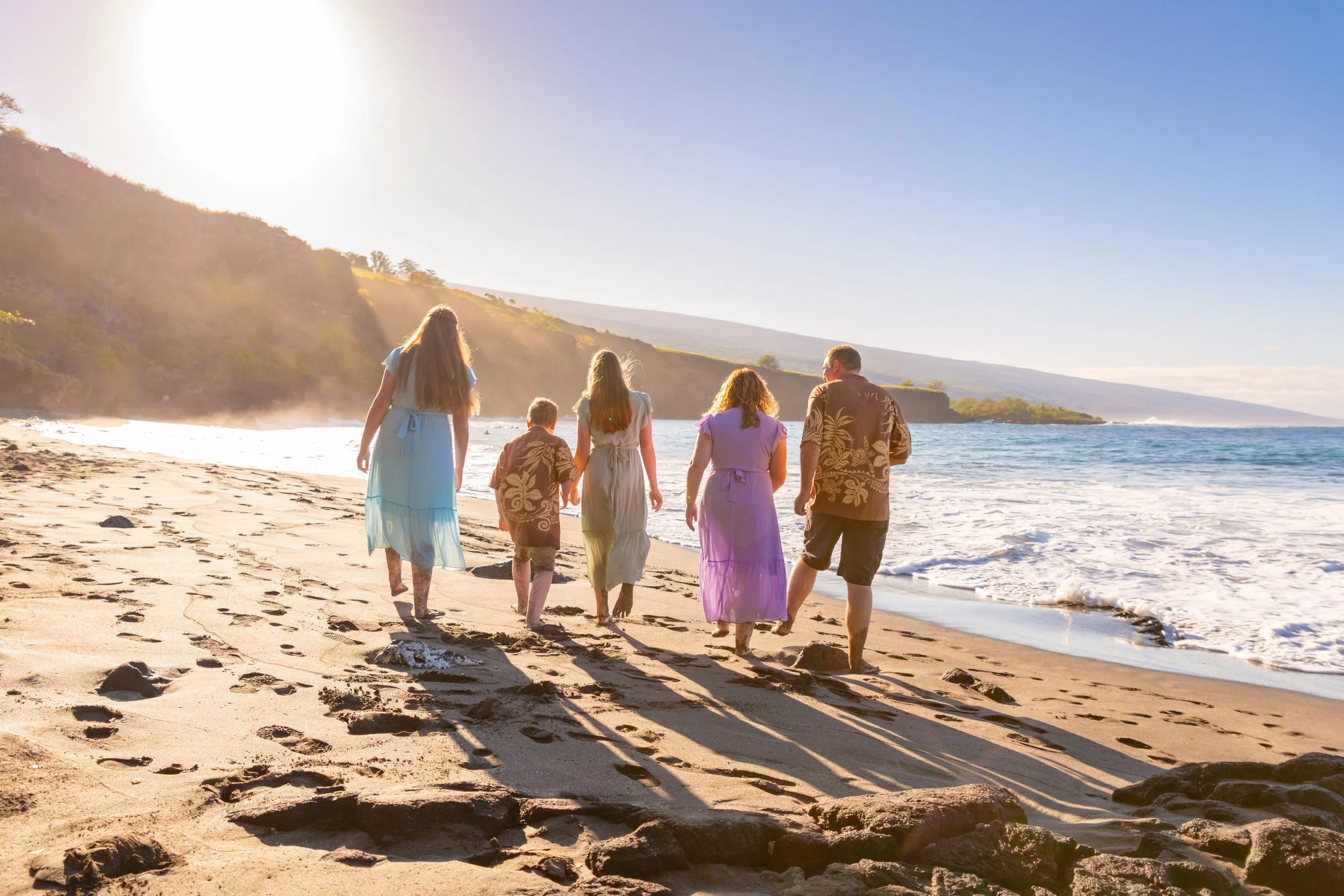 A family of six walking along a sandy beach at sunset, with cliffs in the background.