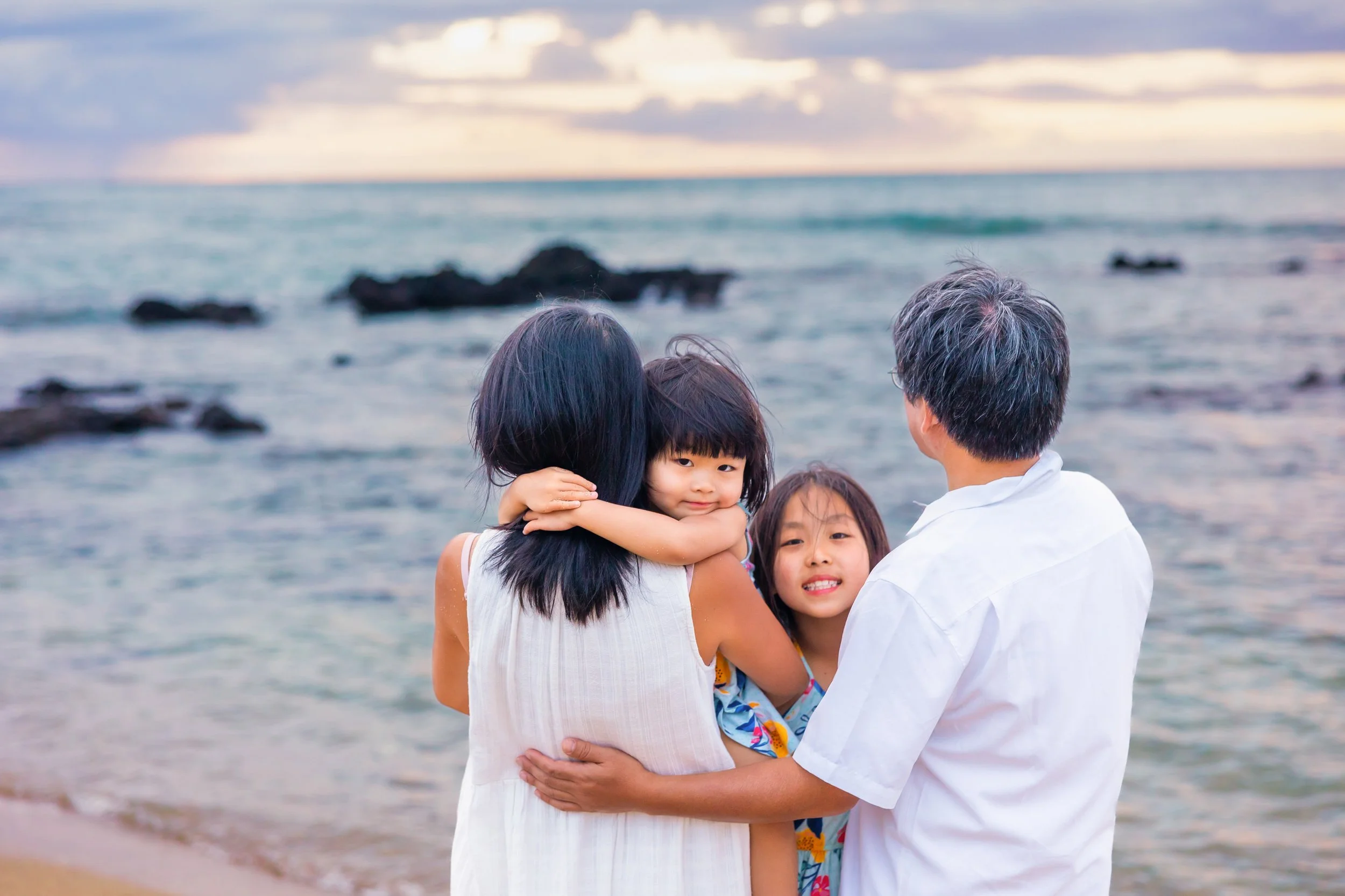 A family of four hugging and enjoying time together on a beach at sunset.