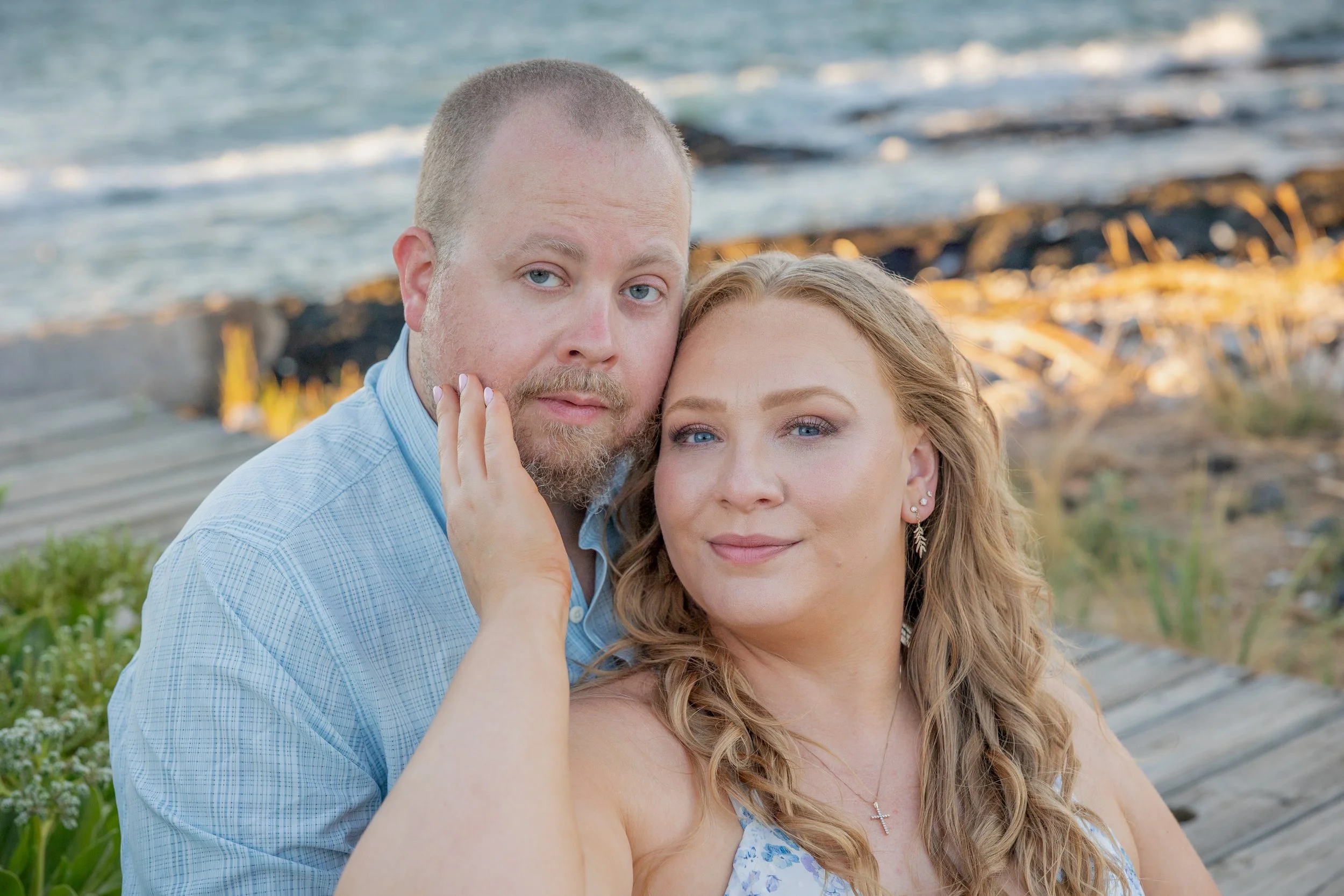 A couple posing by the seaside with waves and rocks in the background.