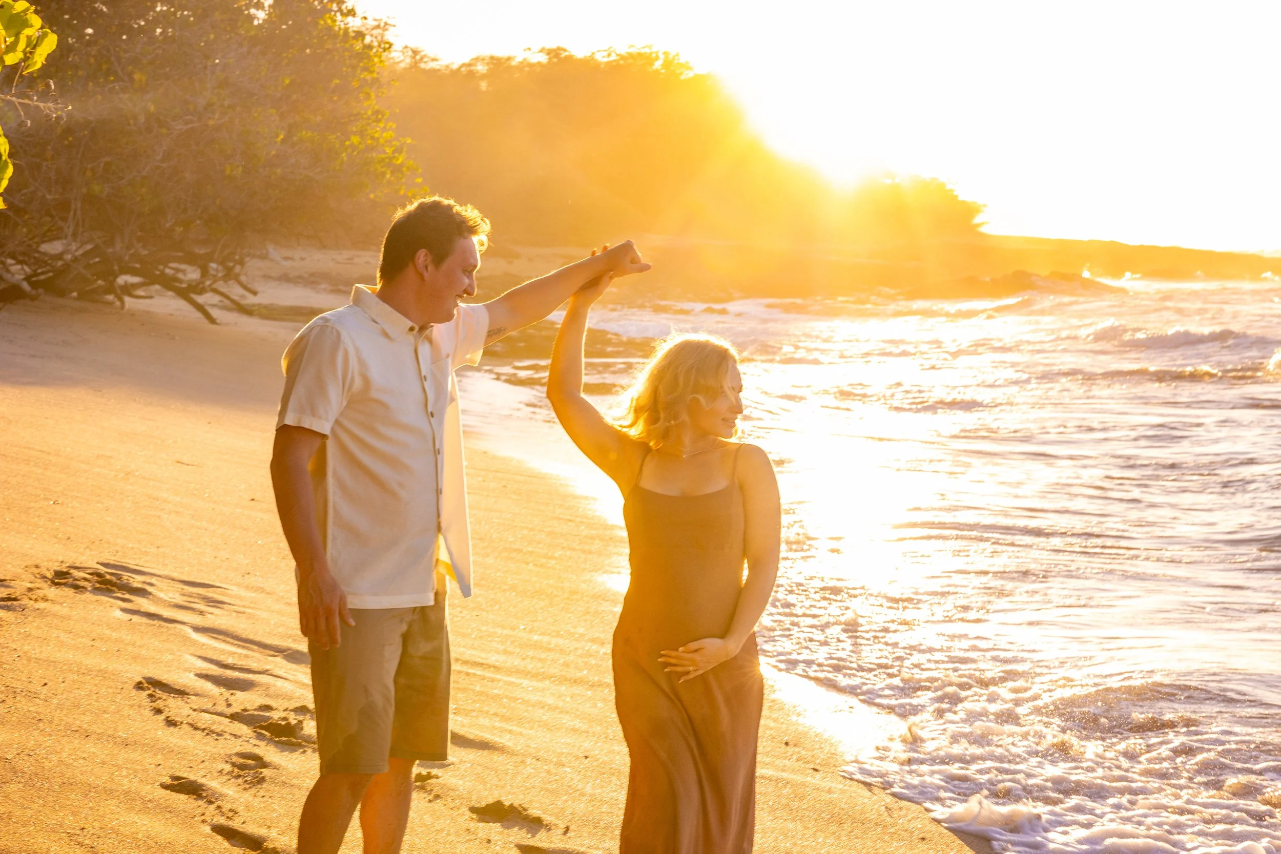 A couple dancing on the beach at sunset, holding hands and smiling.