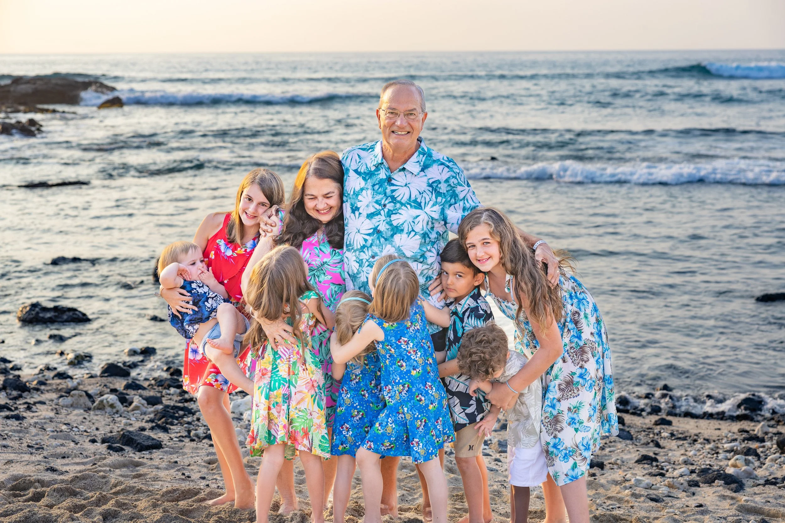 A group of children and an older man in Hawaiian shirts posing on the beach at sunset.
