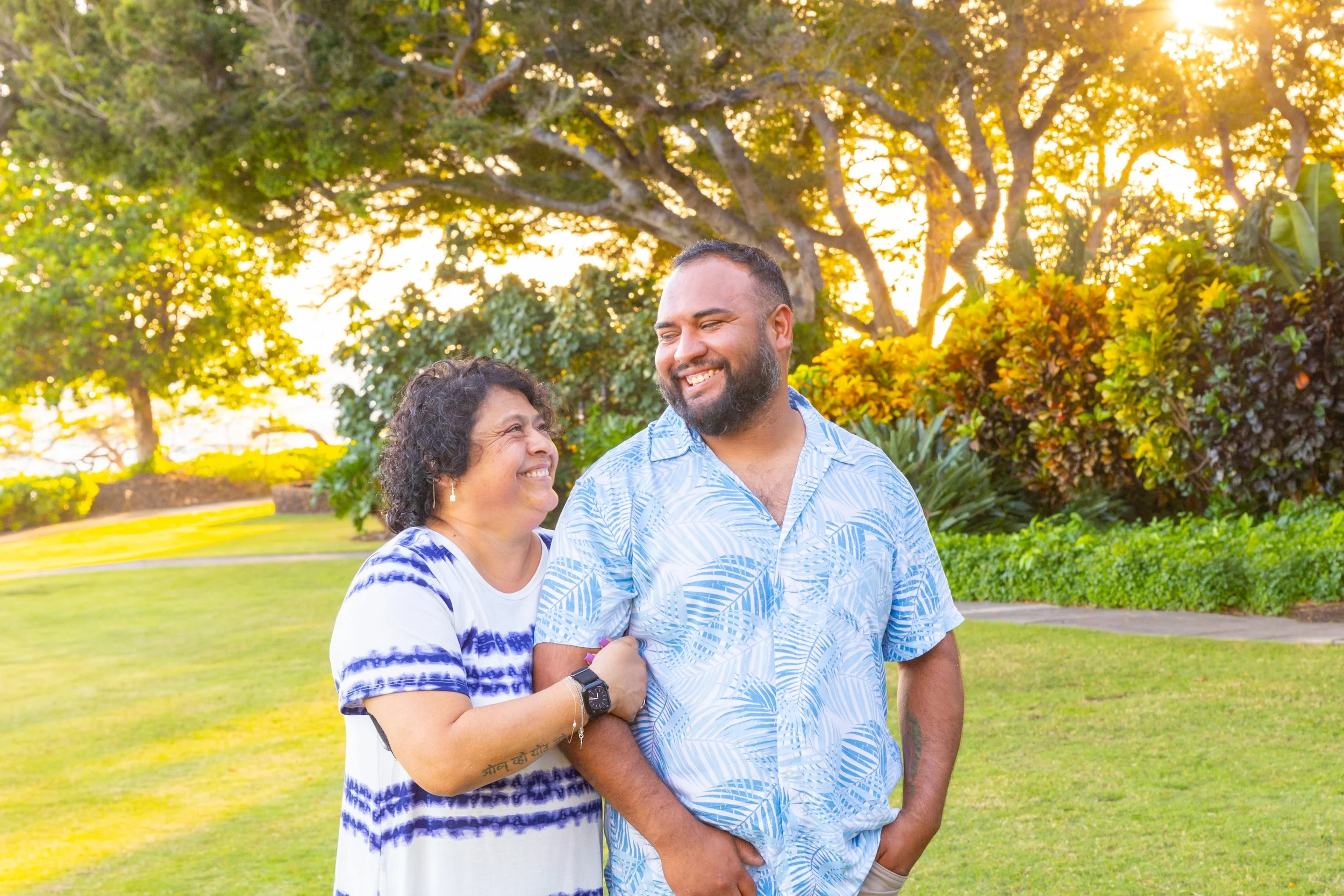 A smiling woman and man enjoying a sunny day outdoors in a park, surrounded by trees and greenery.