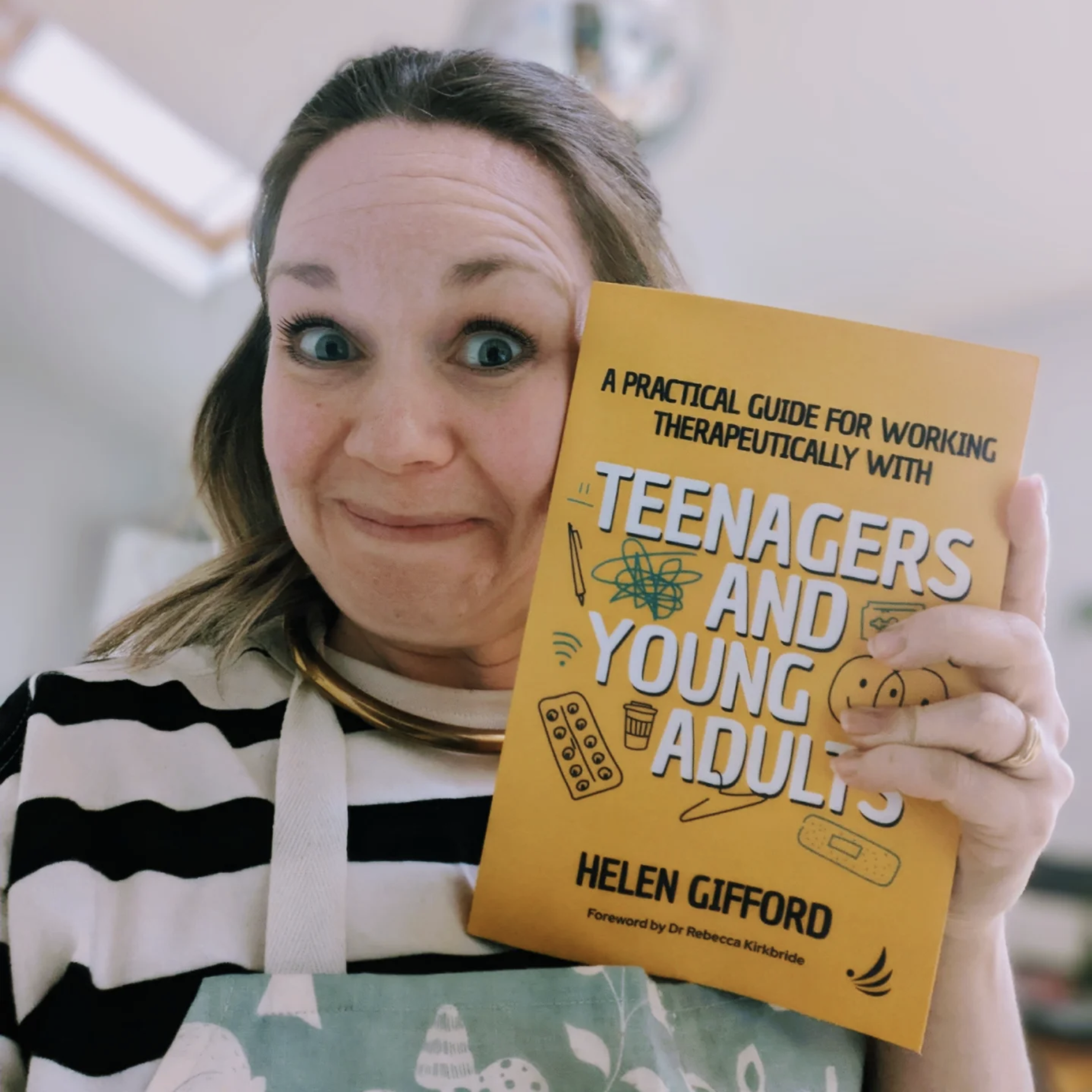 A photo of me, wearing an apron, holding my book with an excited grin