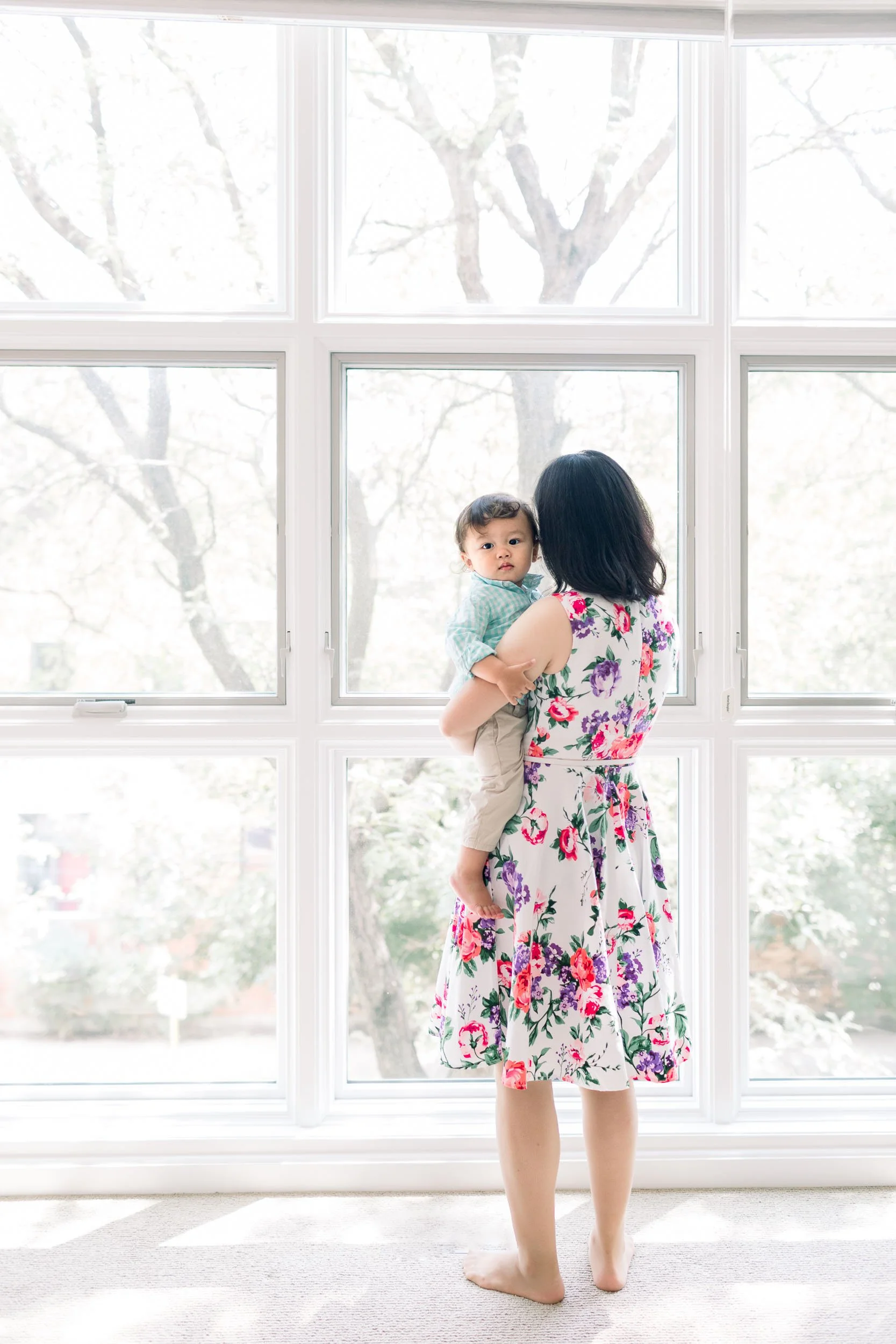 Mother standing by floor-to-ceiling windows and holding baby boy