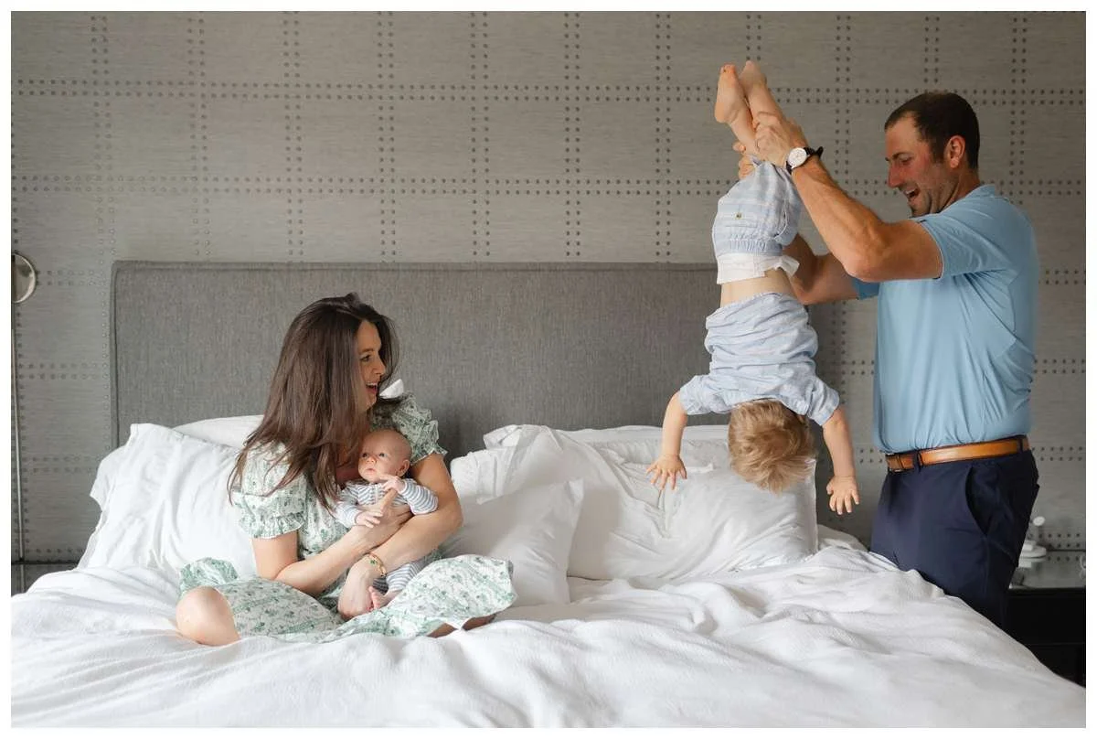 Mom holding baby boy in bed while dad dangles toddler son by his feet