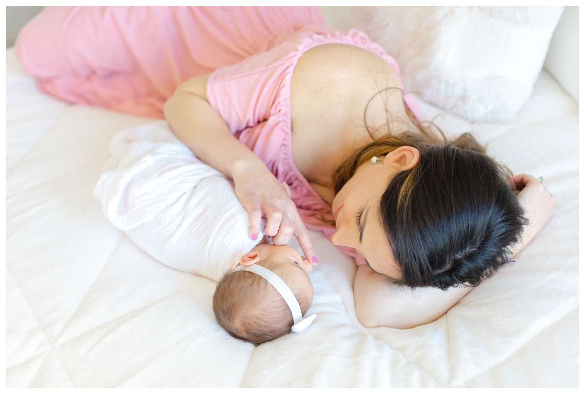 Young mother laying down sideways in bed and touching baby girl's nose in loving gesture 