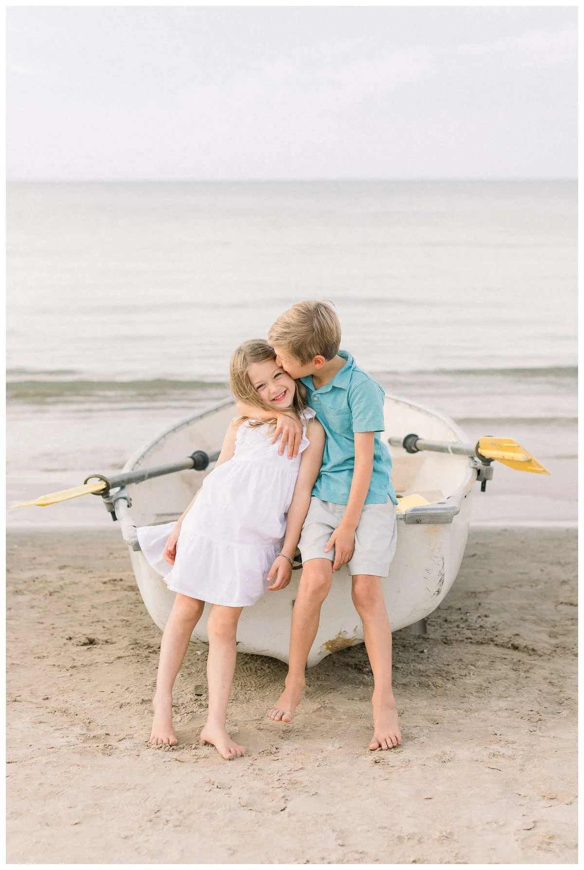 Boy hugging and kissing his sister as they sit on an empty boat in front of Lake Michigan 